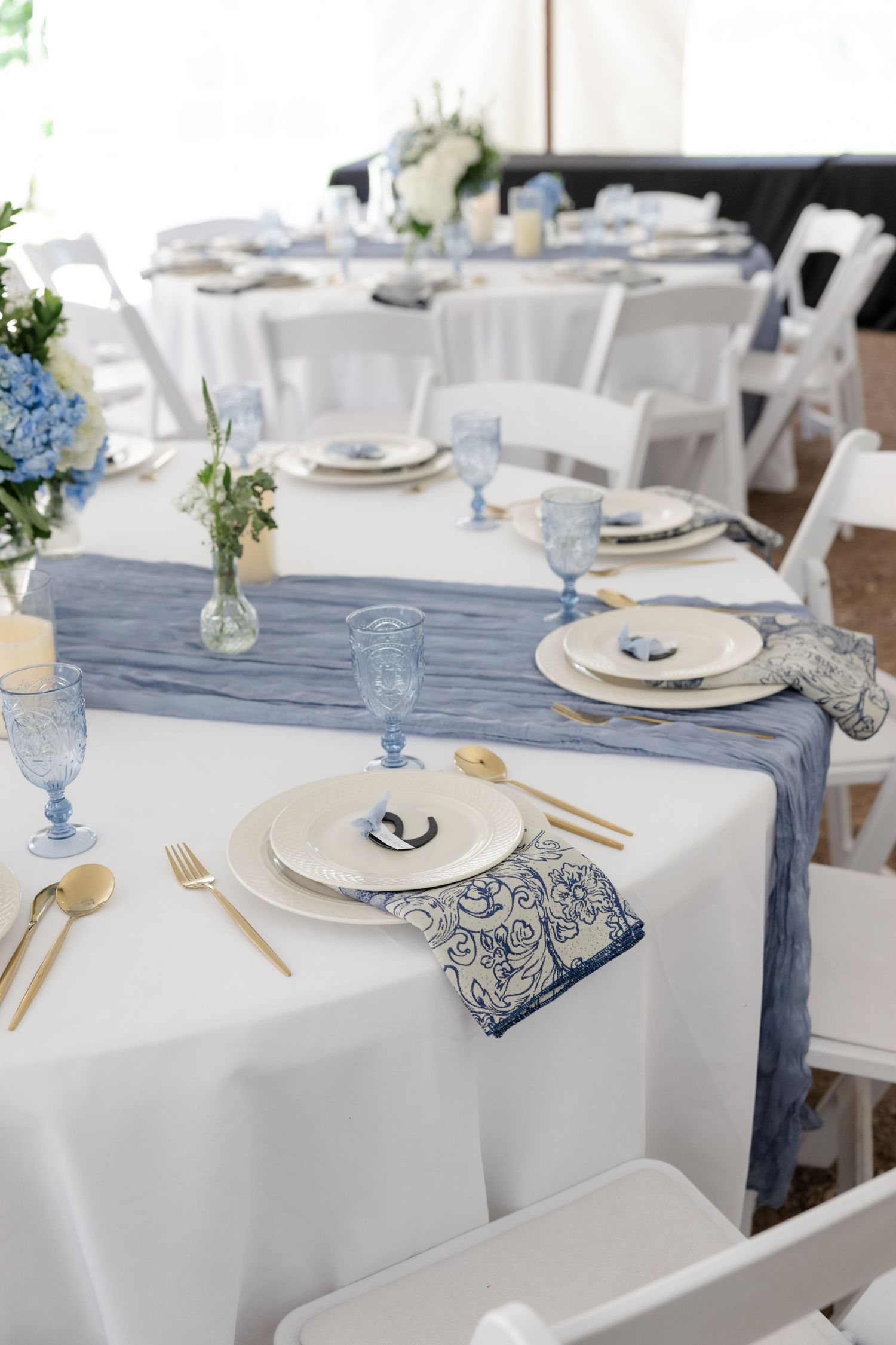 Elegant wedding reception tables set with white linens, blue accents, and delicate floral centerpieces.