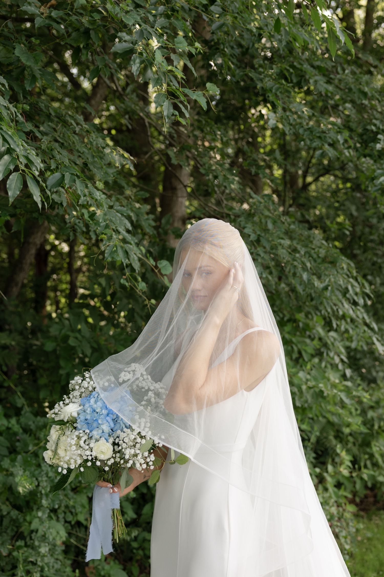 Ethereal bridal portrait showing flowing white veil and baby's breath flowers against green foliage.