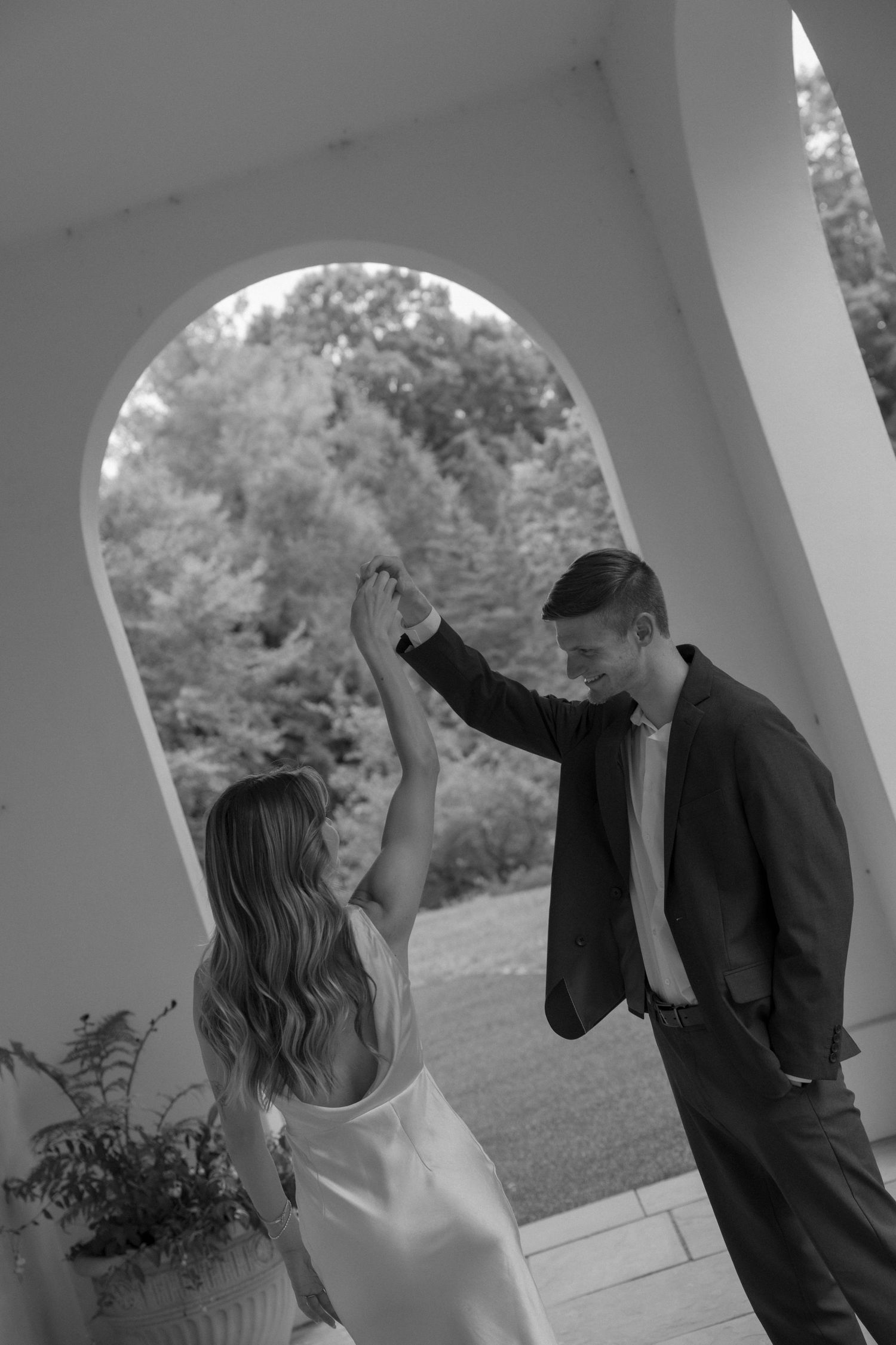 A romantic dance pose under an elegant white archway in black and white.