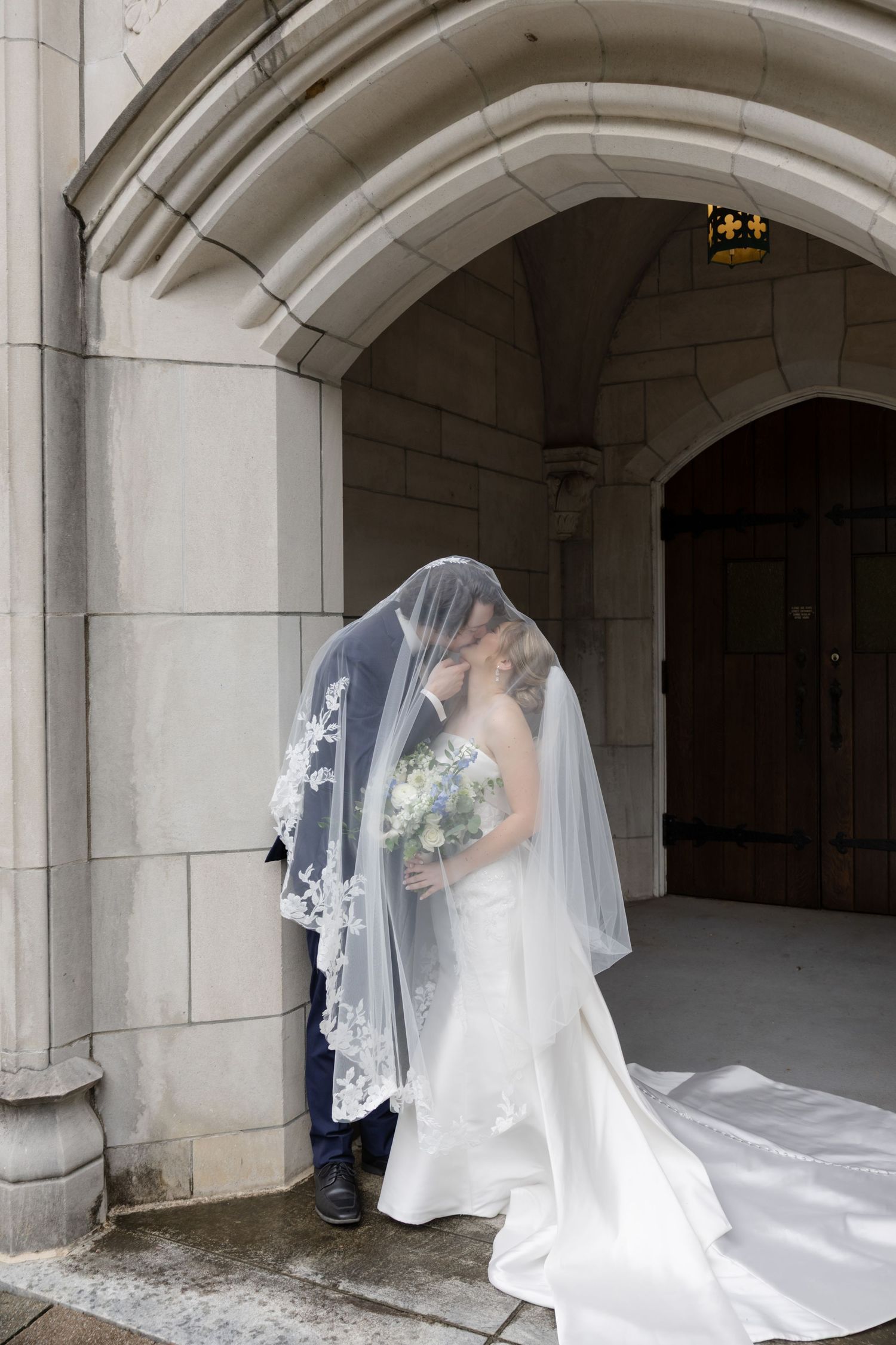 A tender moment between newlyweds under a stone archway with a flowing veil.