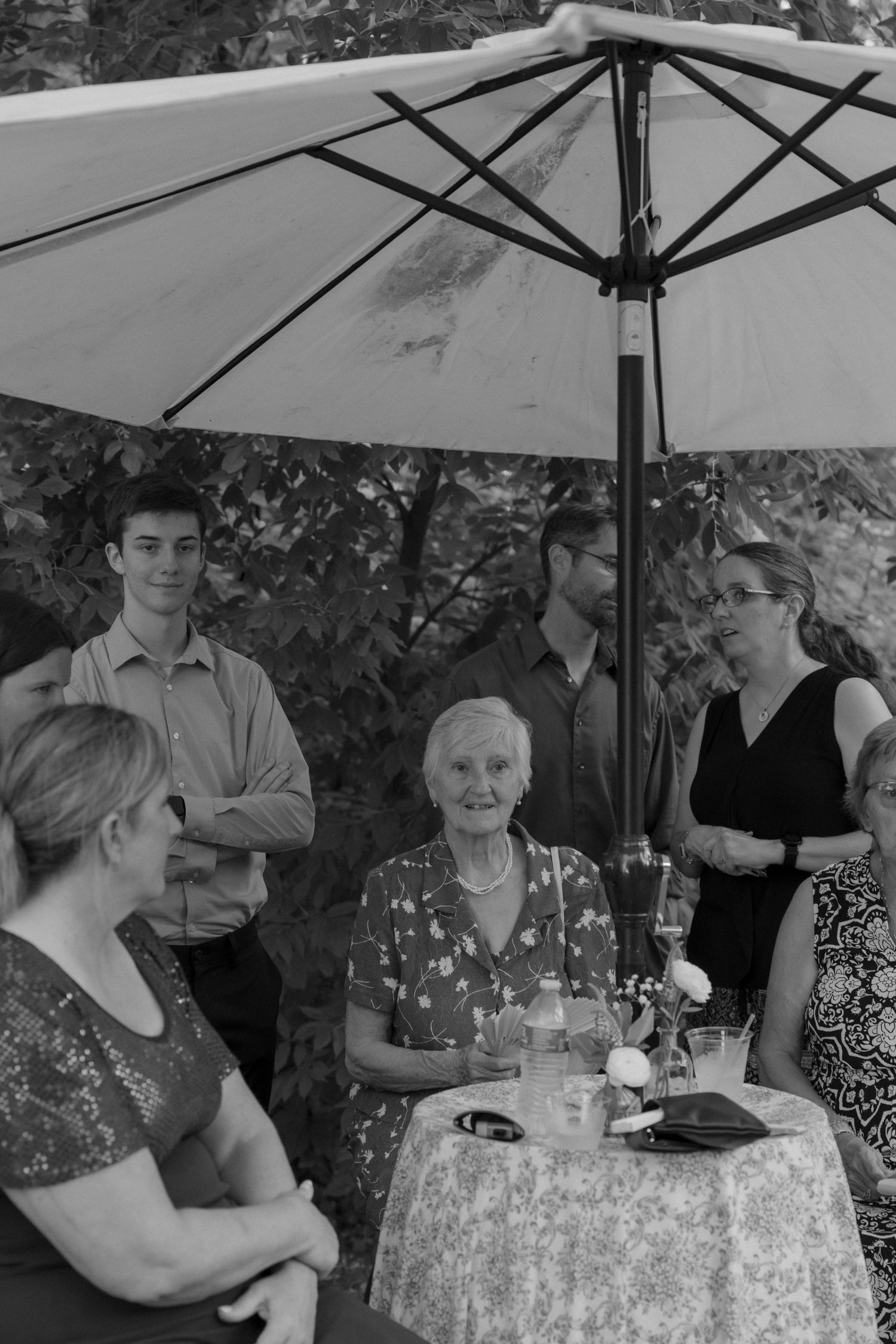 Guests seated under white umbrellas at outdoor tables during a summer event.