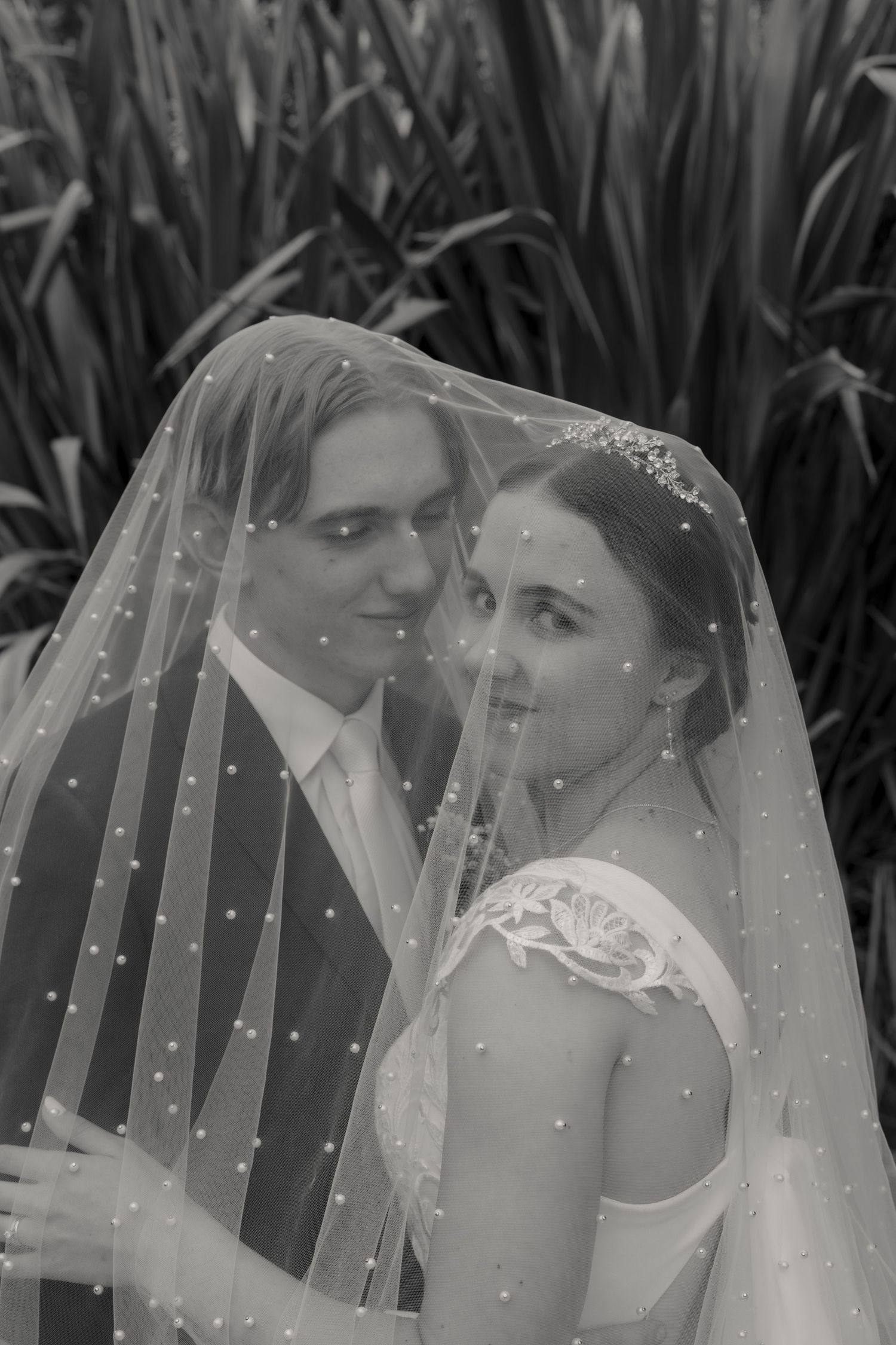 Intimate black and white portrait of couple under dotted wedding veil.