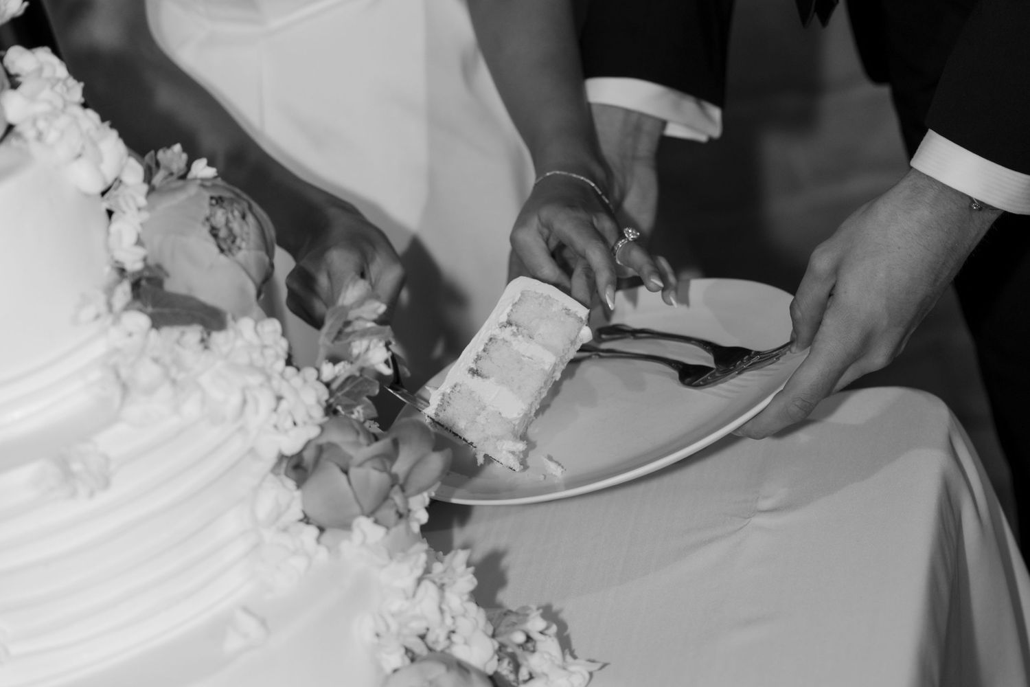 Black and white capture of wedding cake being cut during reception.