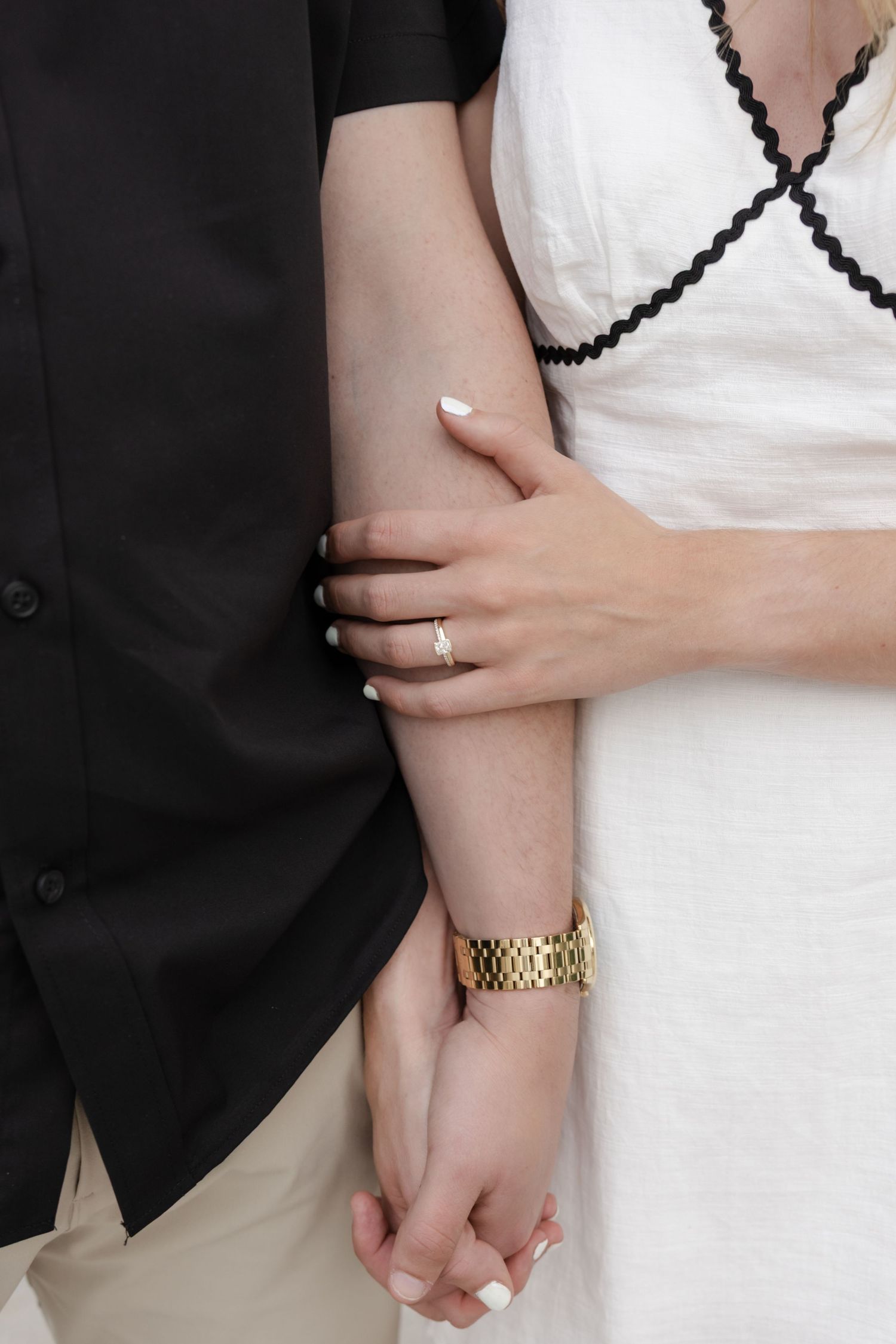 Close-up of embracing couple showing details of white dress and black suit with gold watch.