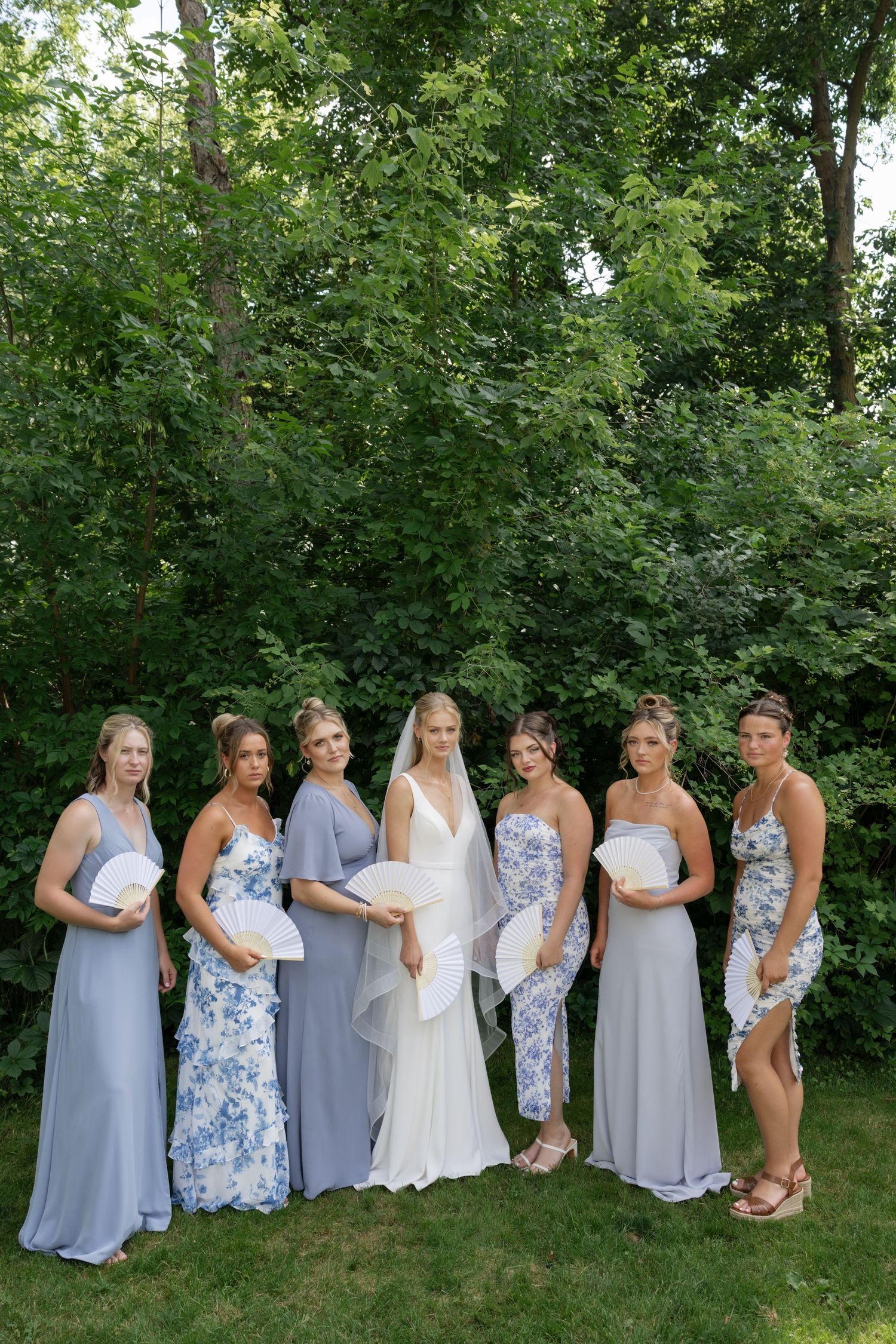 Bridal party wearing light blue and floral dresses poses together in a garden setting.