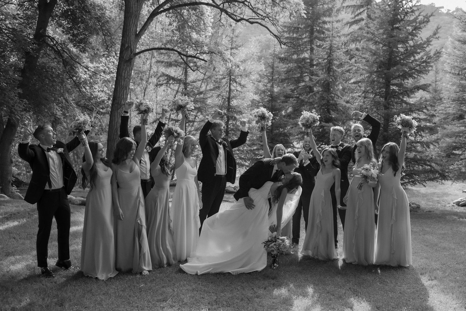 Wedding party lined up for formal photos against a backdrop of evergreen trees.