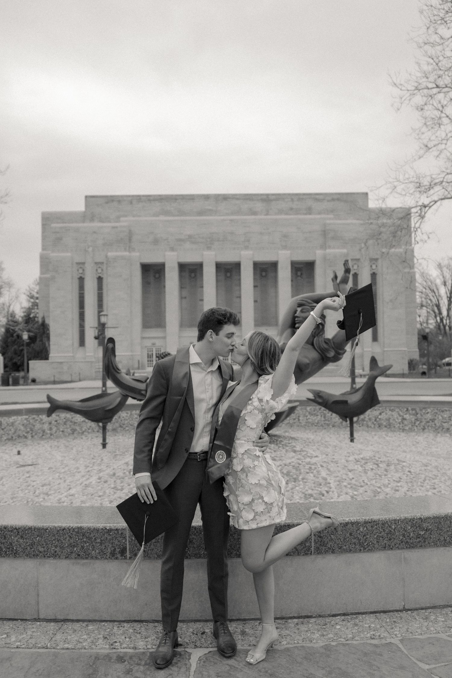 Three playful graduation poses shown in black and white in front of a collegiate building.