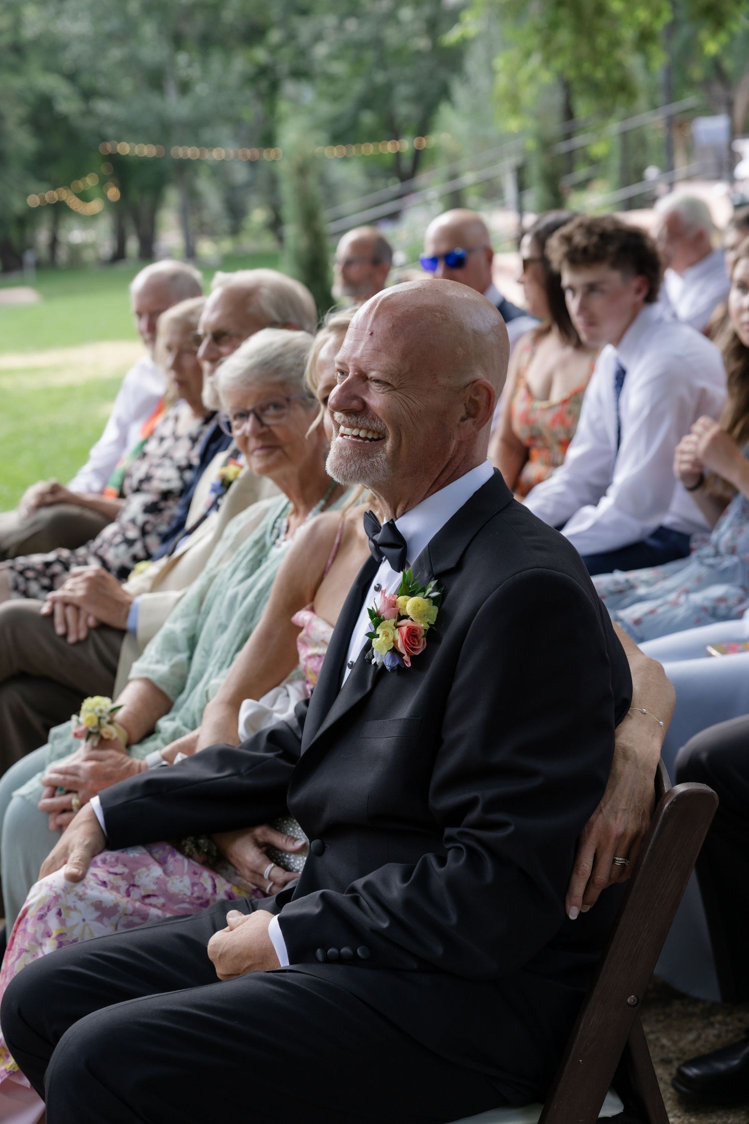 Wedding guests enjoying the ceremony from wooden chairs in an outdoor setting.