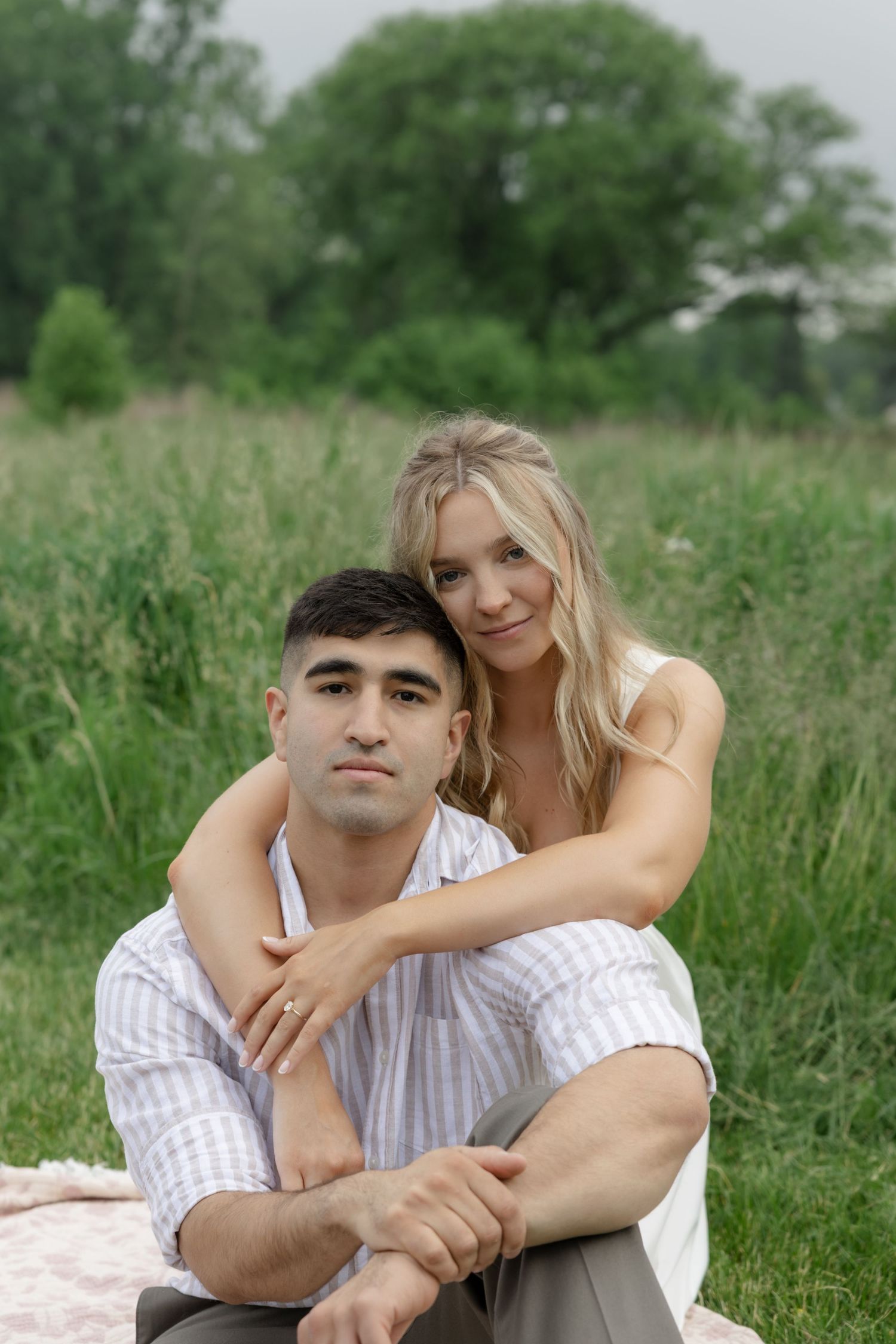 A couple shares an intimate moment while laying together in a grassy field on a sunny day.