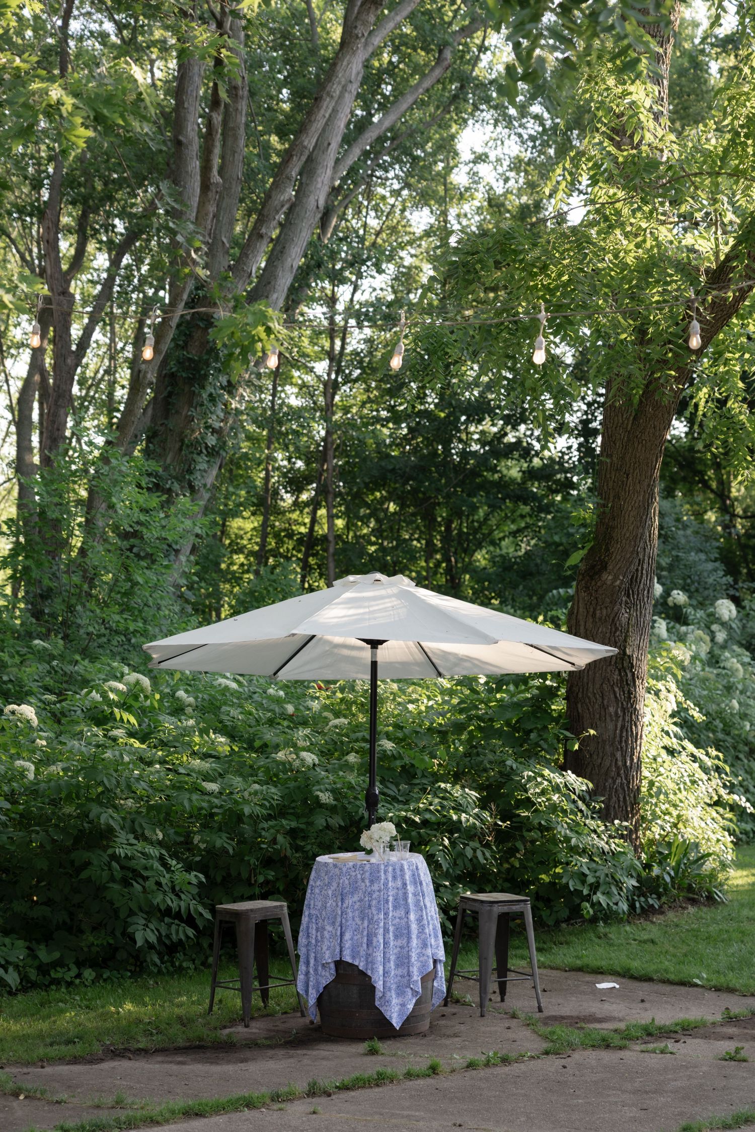 A peaceful garden setting with a white umbrella and tablecloth over a small table.