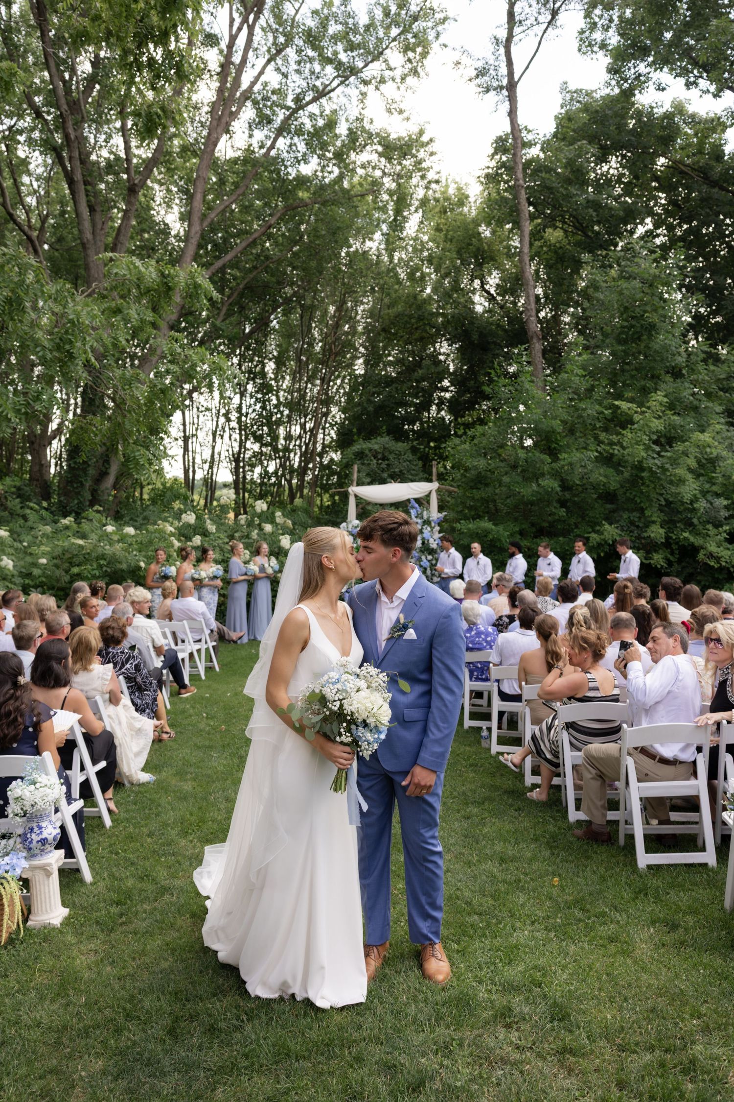 Wedding recessional with guests seated on white chairs as couple walks down grassy aisle.