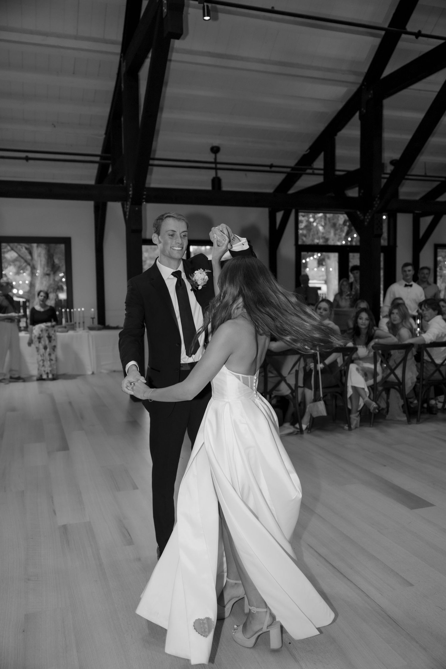 Couple performs their first dance in rustic venue with exposed wooden beams.