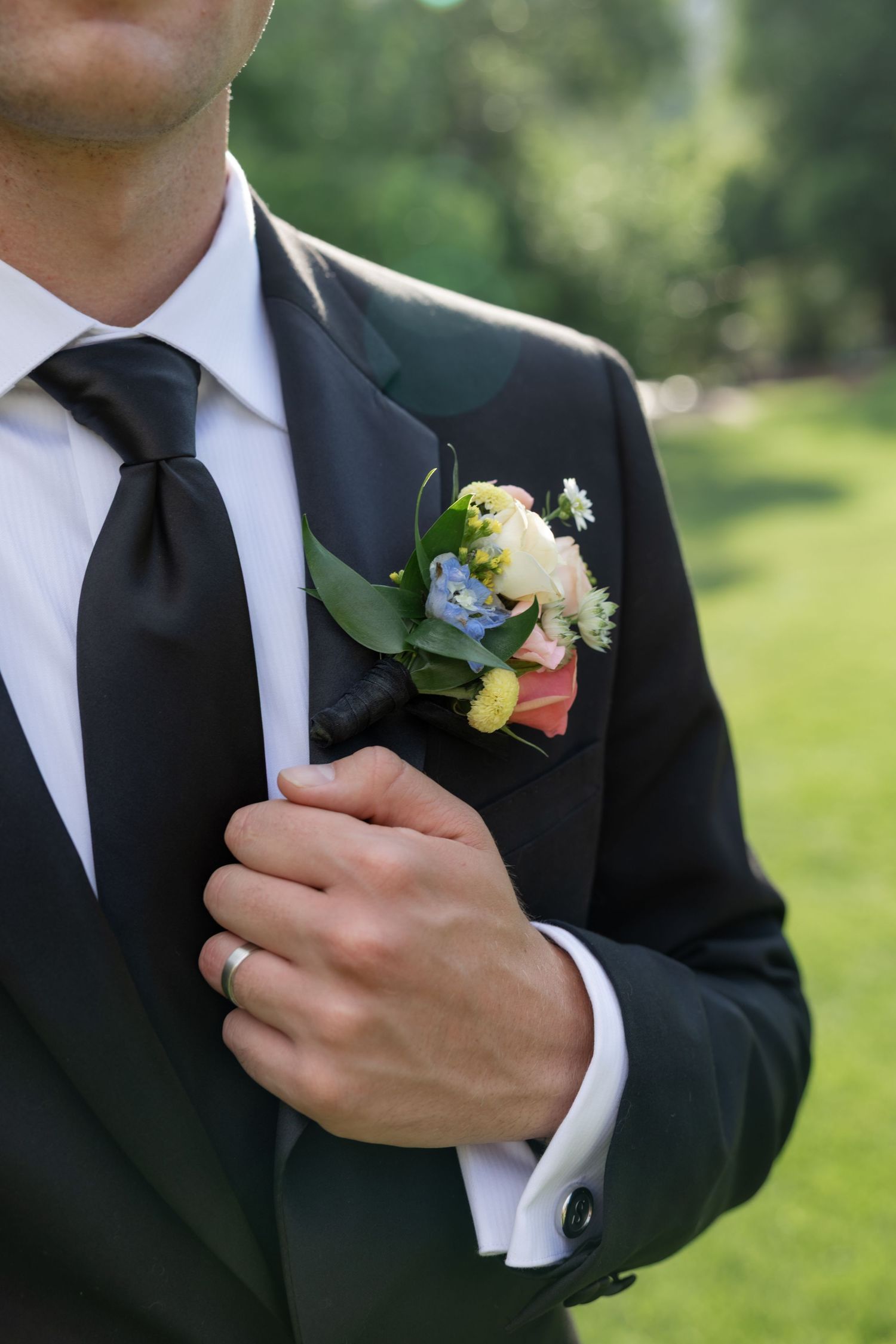 Close-up of groom's boutonniere with delicate flowers against black suit.