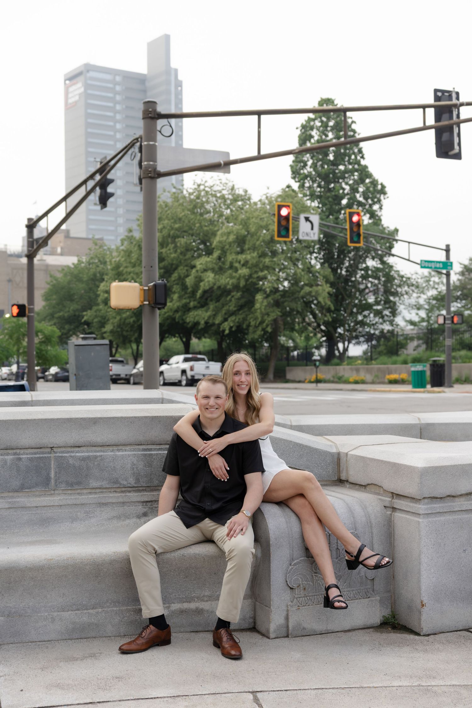 Couple sitting casually together on concrete steps in an urban setting with traffic lights in background.