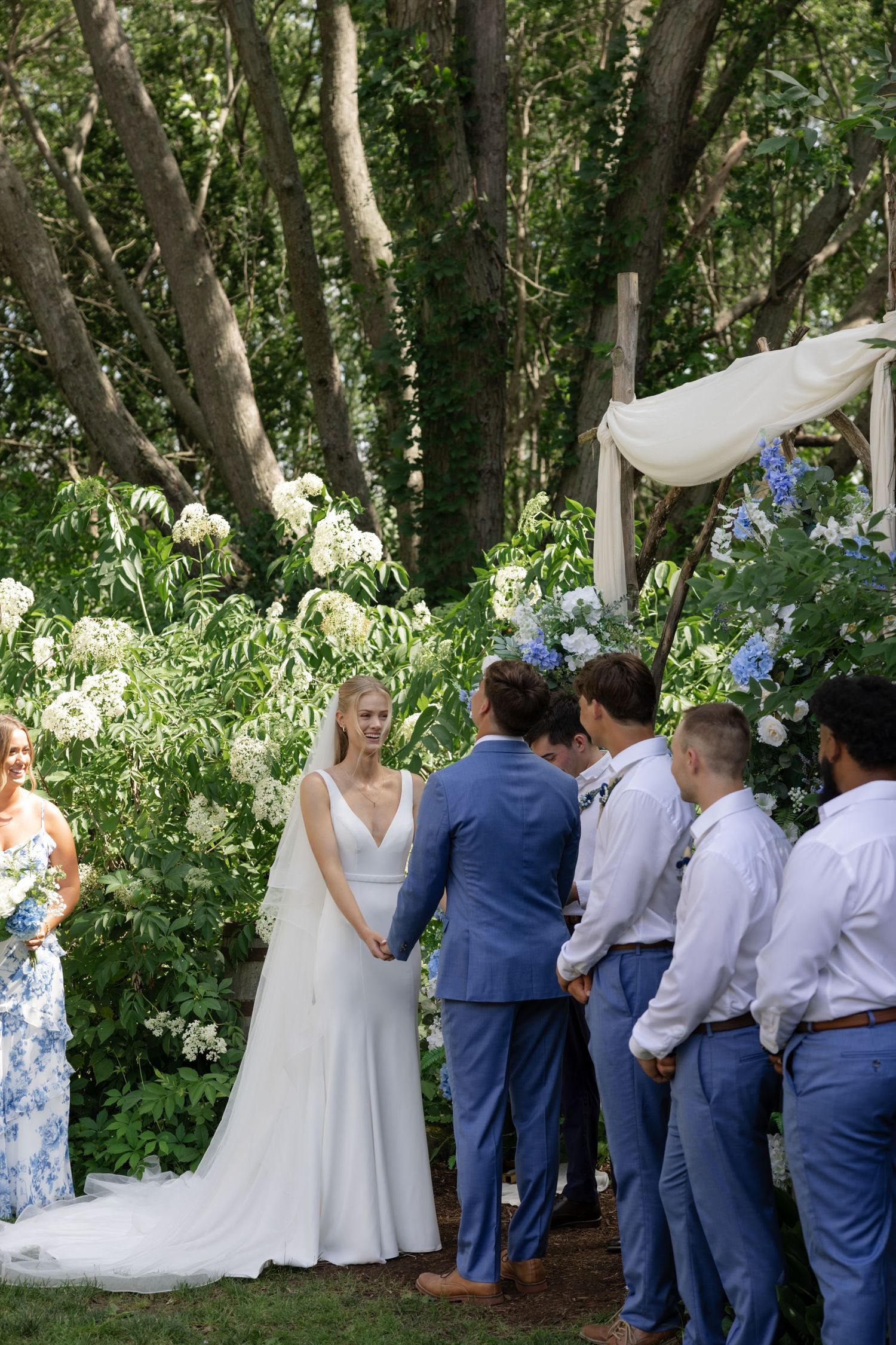 Wedding ceremony moment captured in a wooded outdoor setting with floral decorations.
