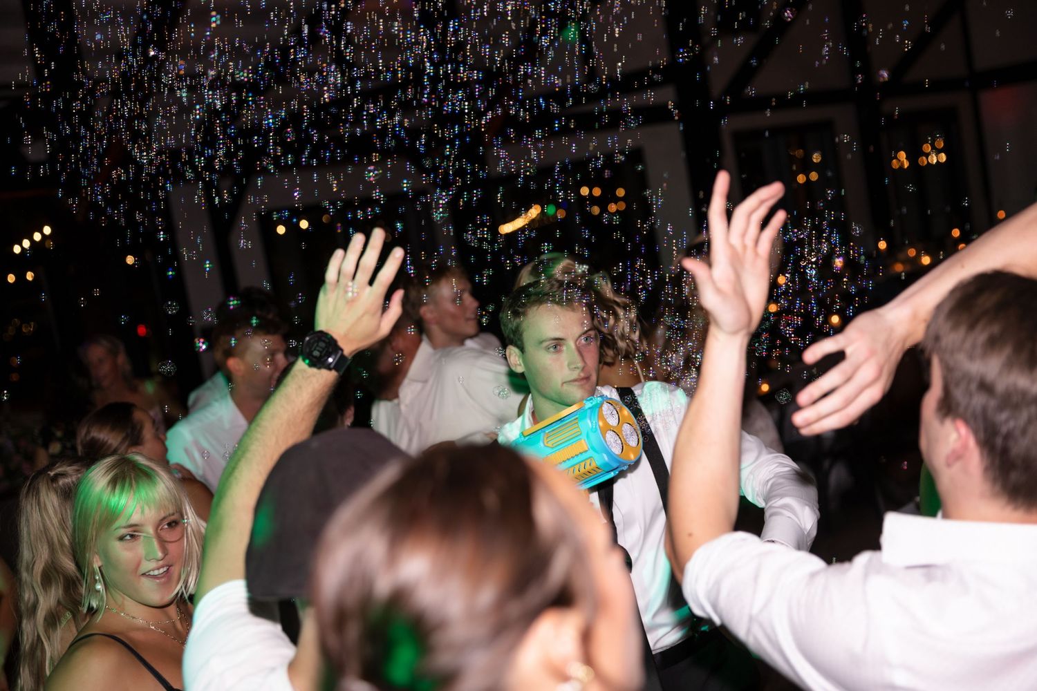 Wedding guests dancing enthusiastically with raised hands on a dark dance floor.