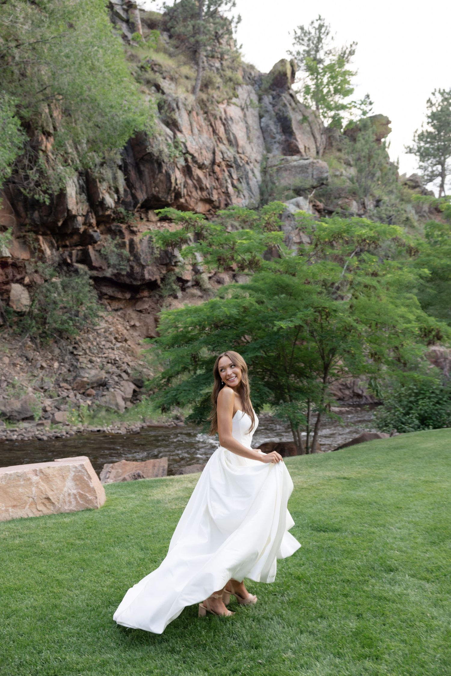 Bride twirls white wedding dress against dramatic rocky cliff backdrop.