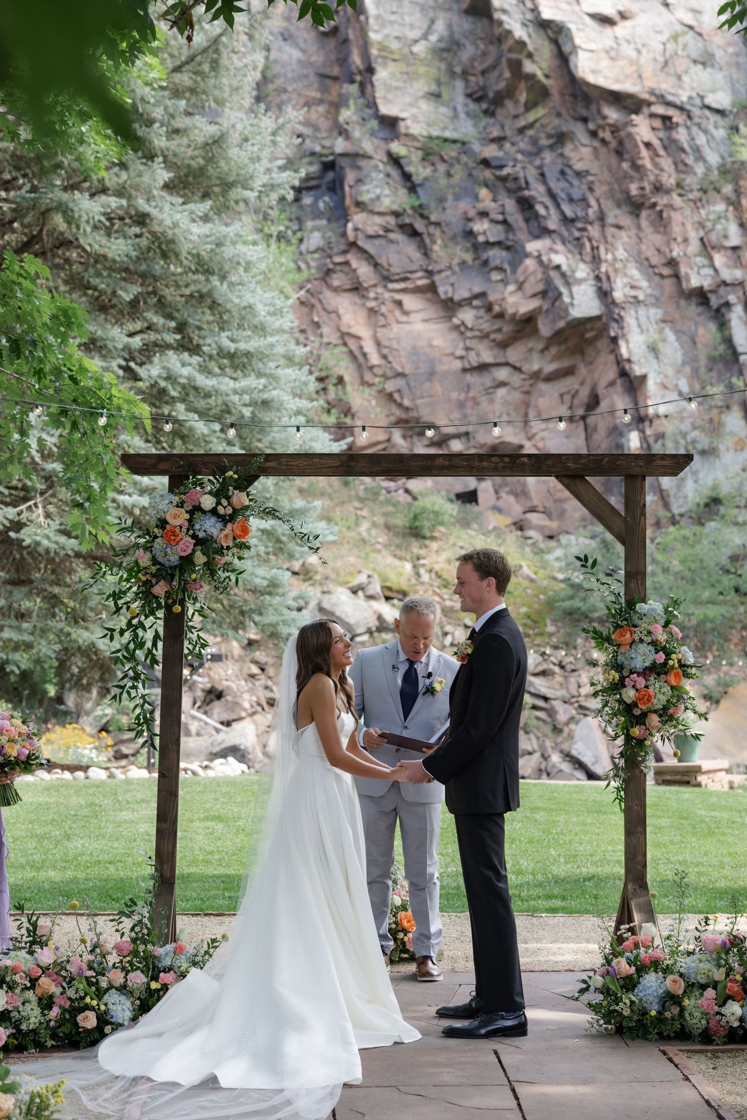 Wedding ceremony progression shots under wooden arch with mountain backdrop.