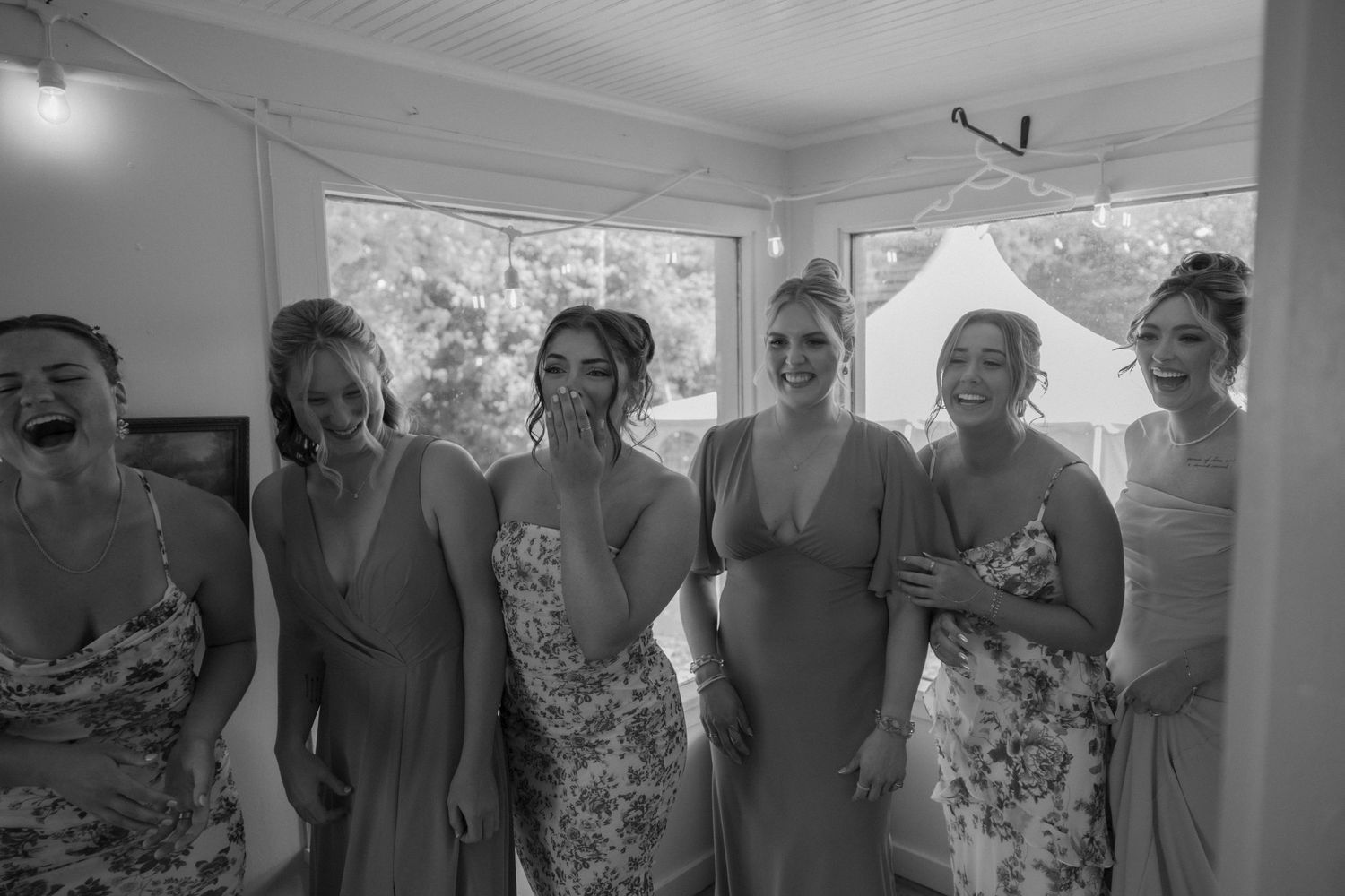 Wedding party in blue floral dresses gather in a sunlit room.