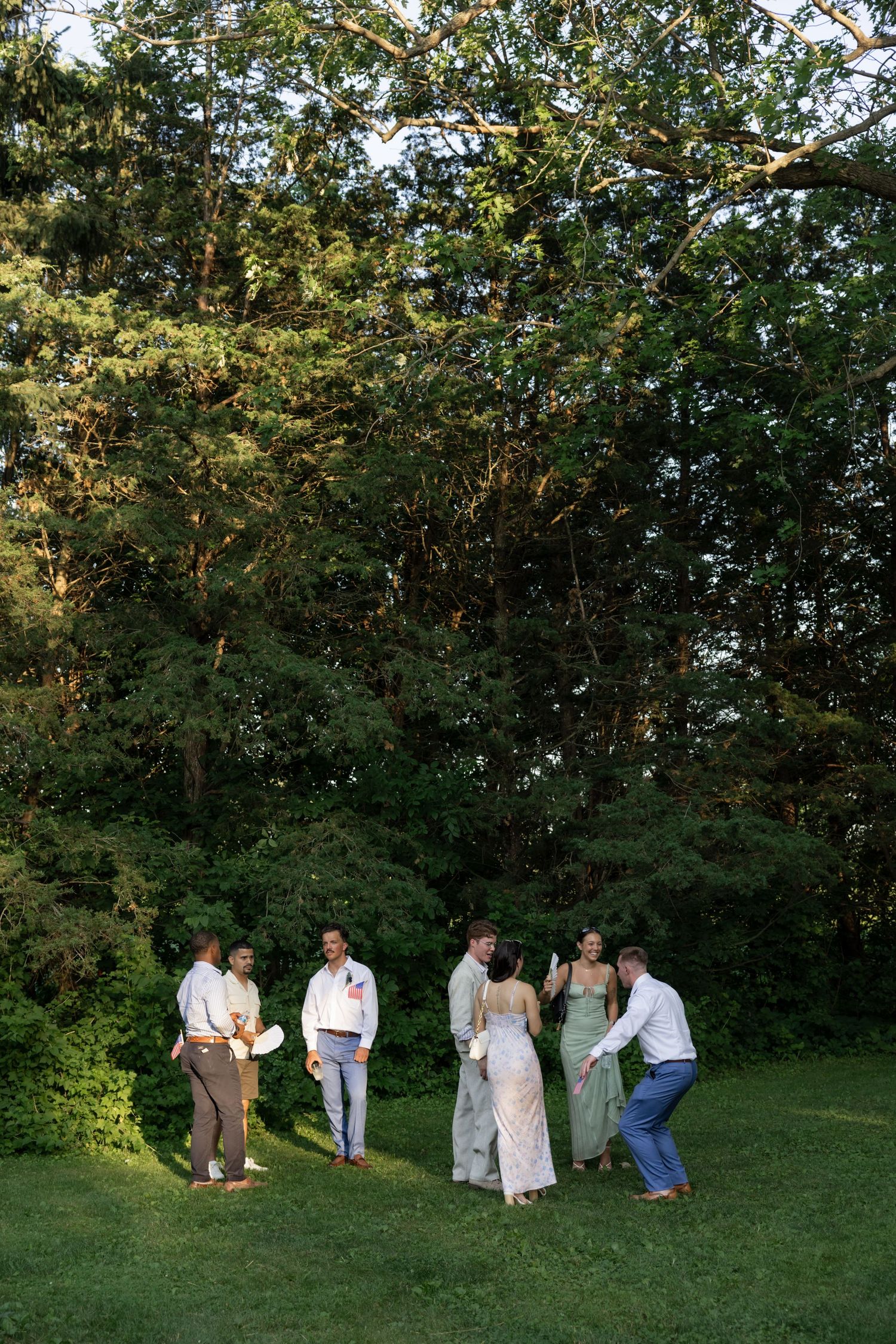 Wedding party posing for group photos on a grassy hillside during golden hour.
