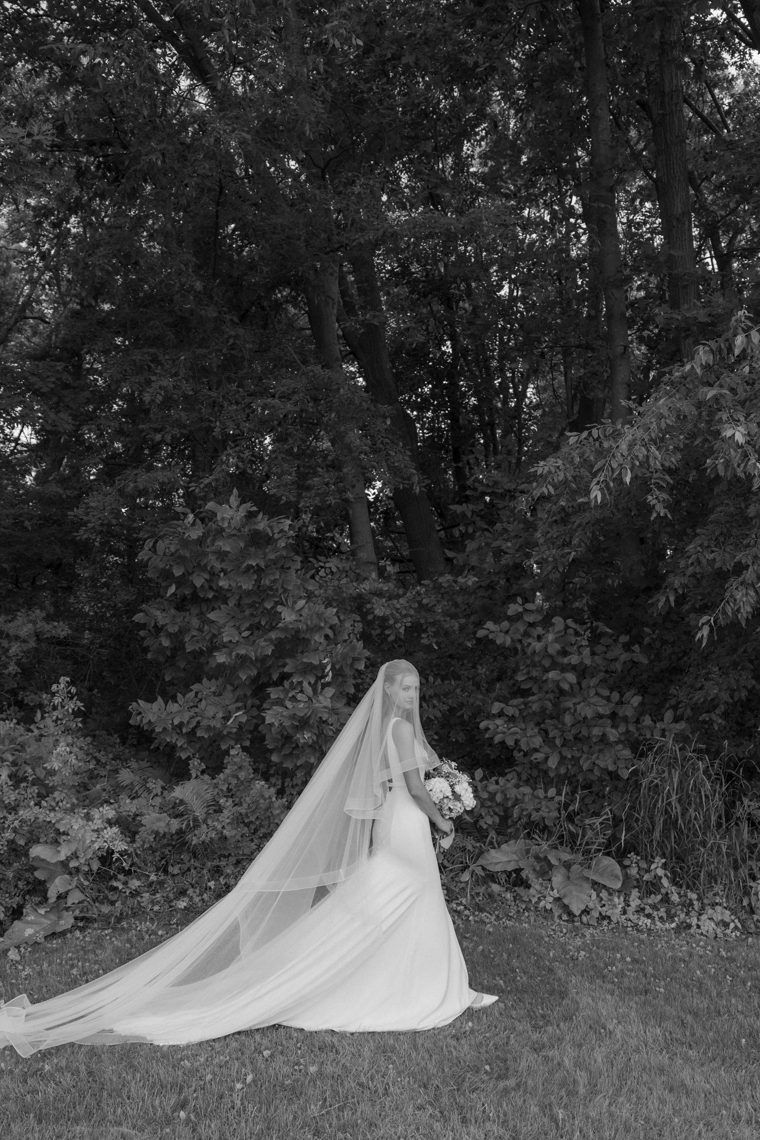 Flowy white wedding veil flowing gracefully across a grassy outdoor area in a series of black and white photos.