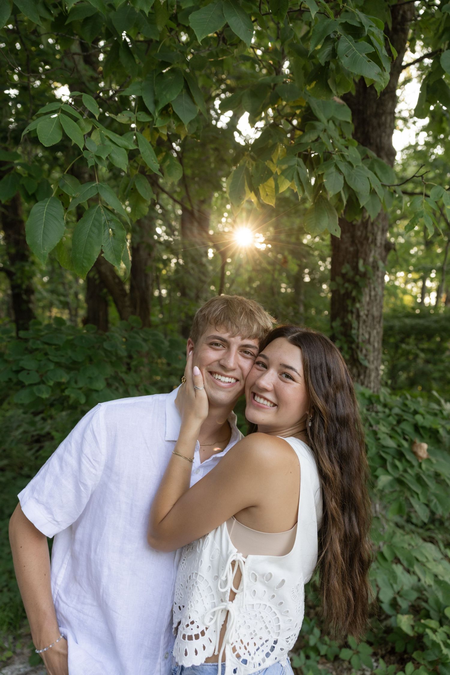 A joyful couple in white outfits laughing together in a lush green forest setting.