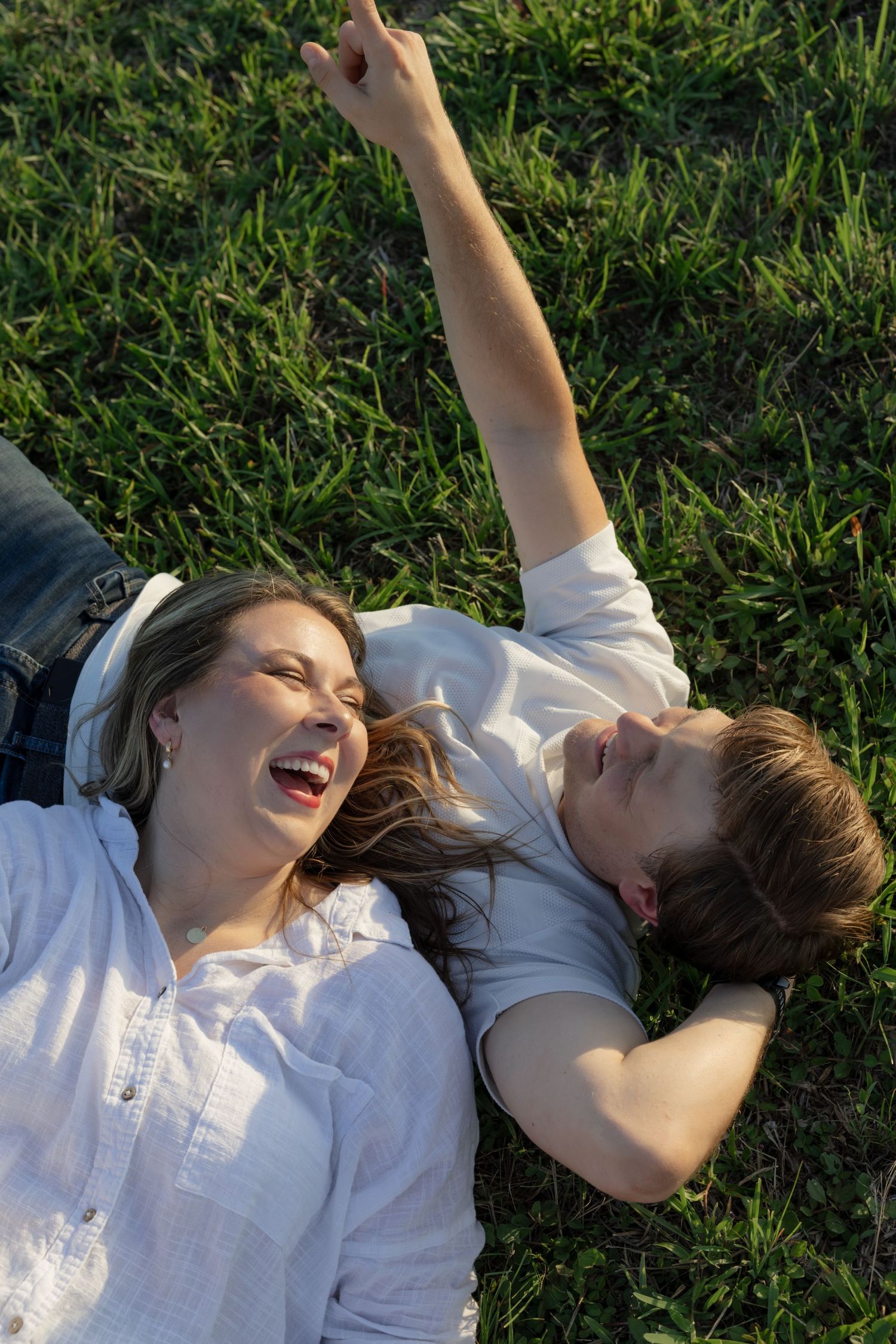 Two people lying in grass laughing and pointing at the sky.