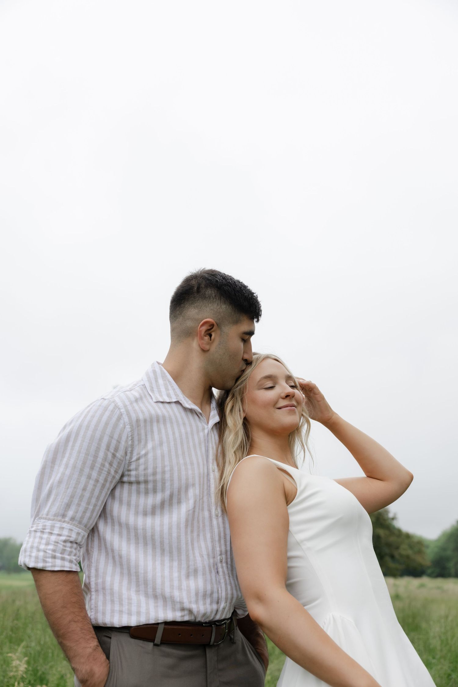 A couple shares an intimate moment together in a grassy field on a cloudy day.