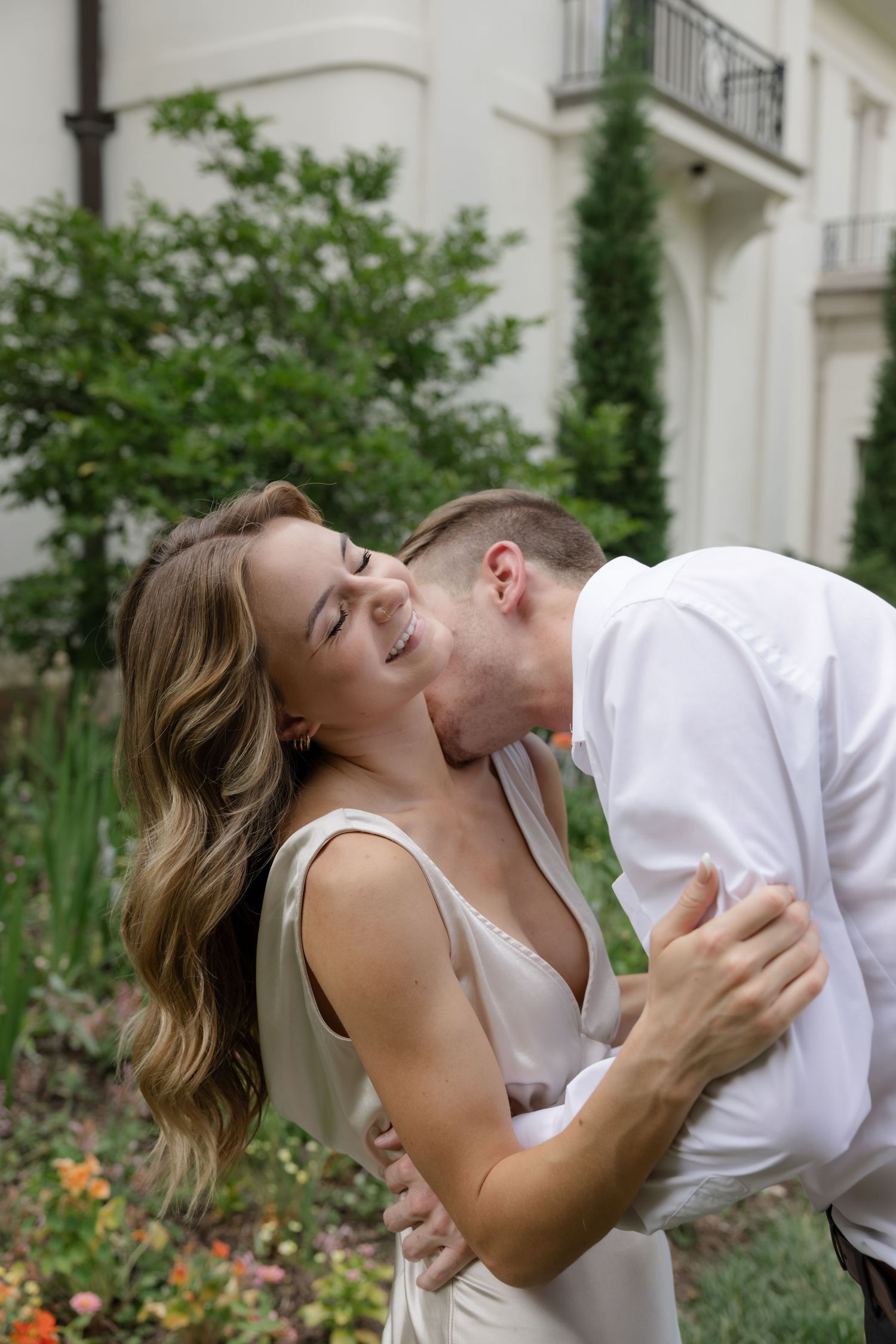 A tender moment captured between a couple in a garden setting with white architecture.