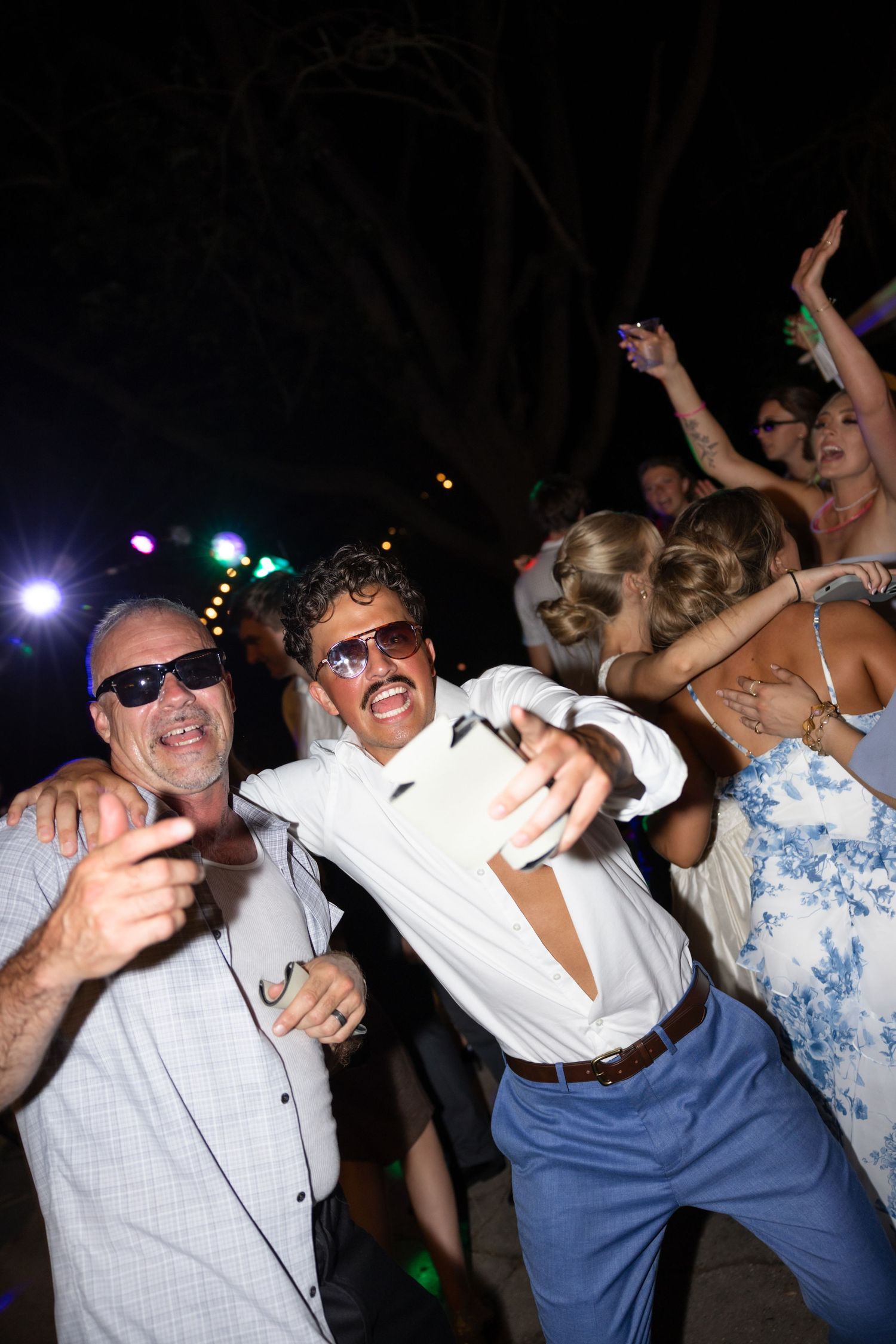 Energetic dancers celebrate at a nighttime party with colorful lighting effects.