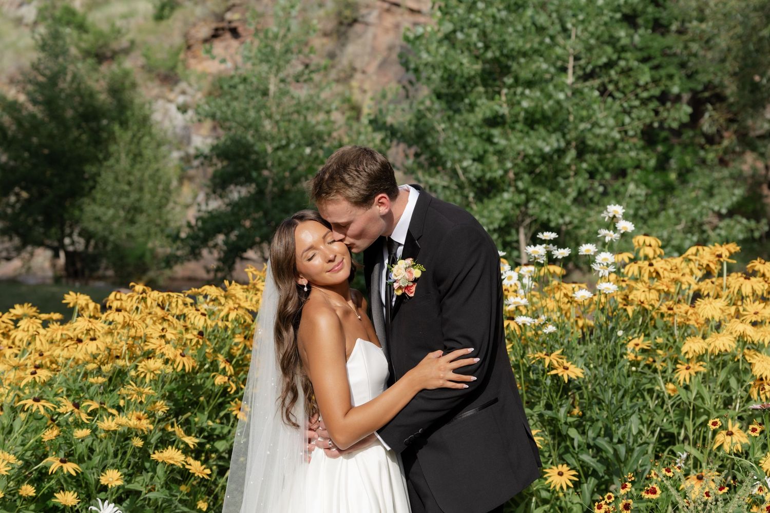 Wedding couple poses among vibrant yellow flowers in outdoor garden.