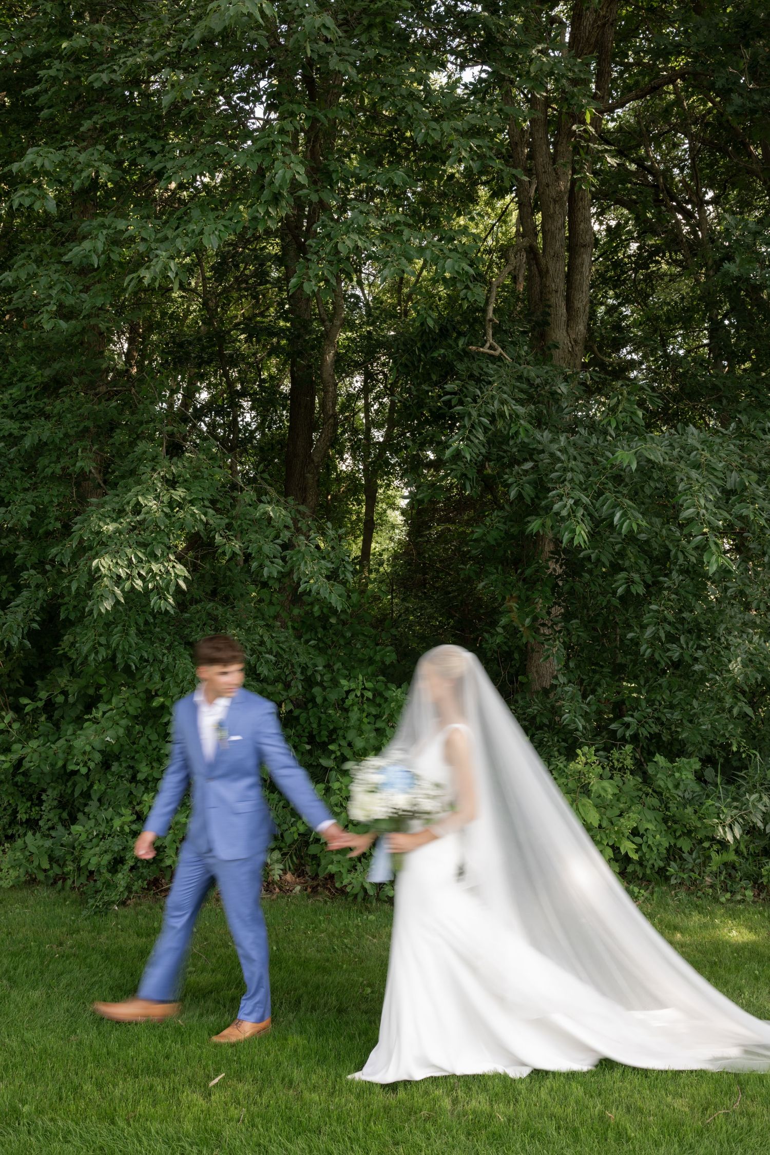 Playful wedding couple dancing and twirling in a green garden setting.