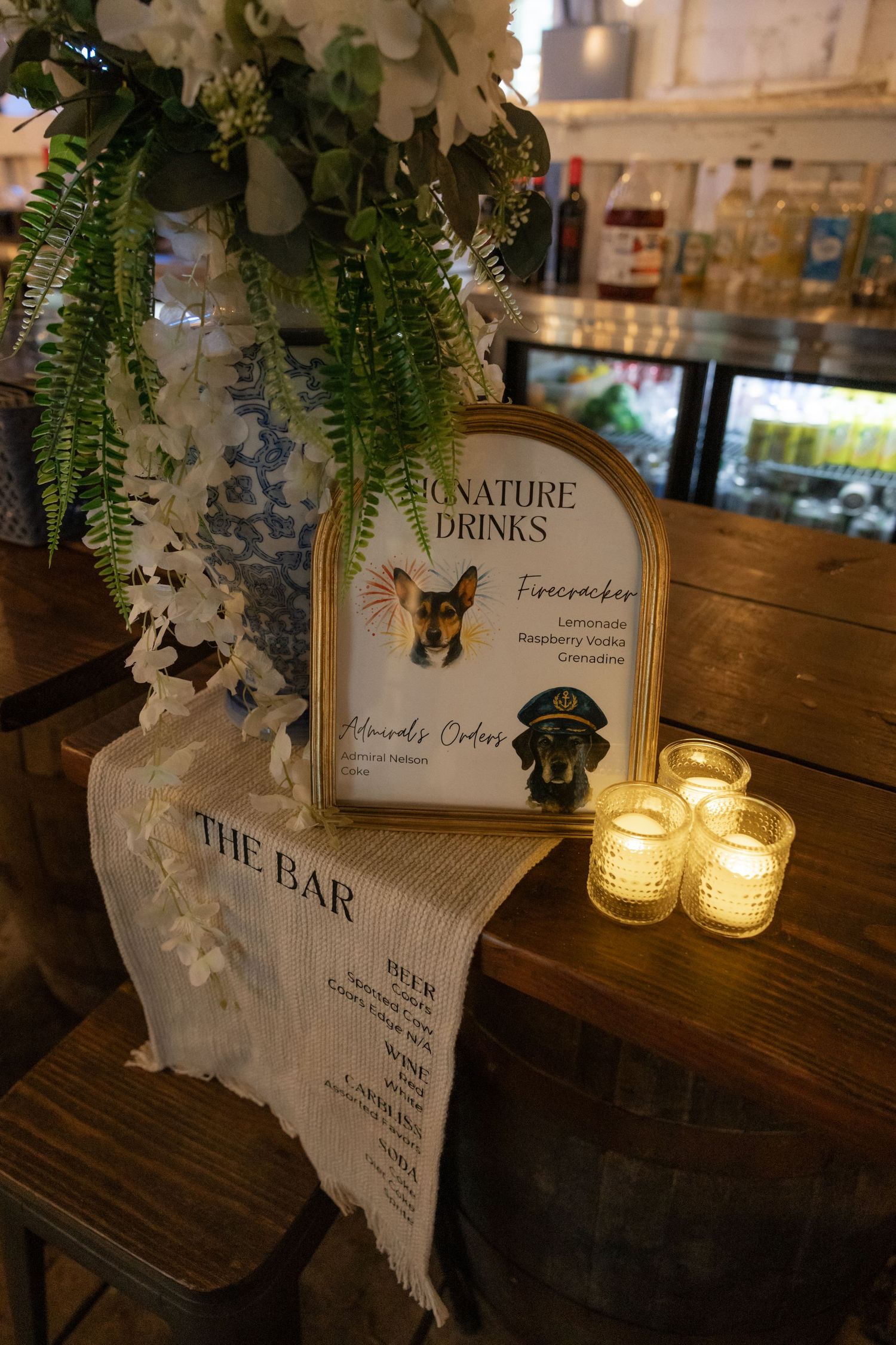 Wedding bar menu signs and candles displayed on rustic wooden surface with floral decorations.