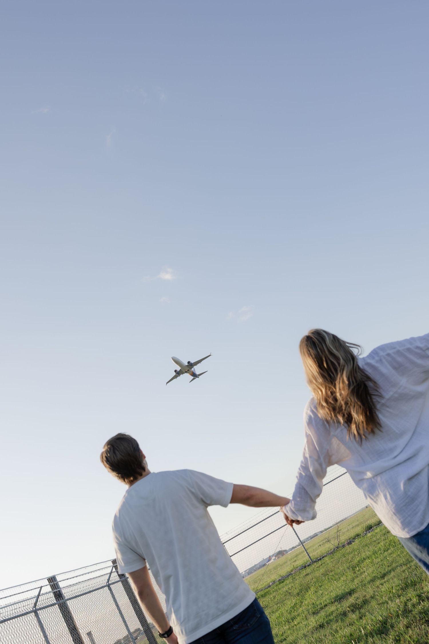 People watching airplanes fly over a green field with a fence in the background.