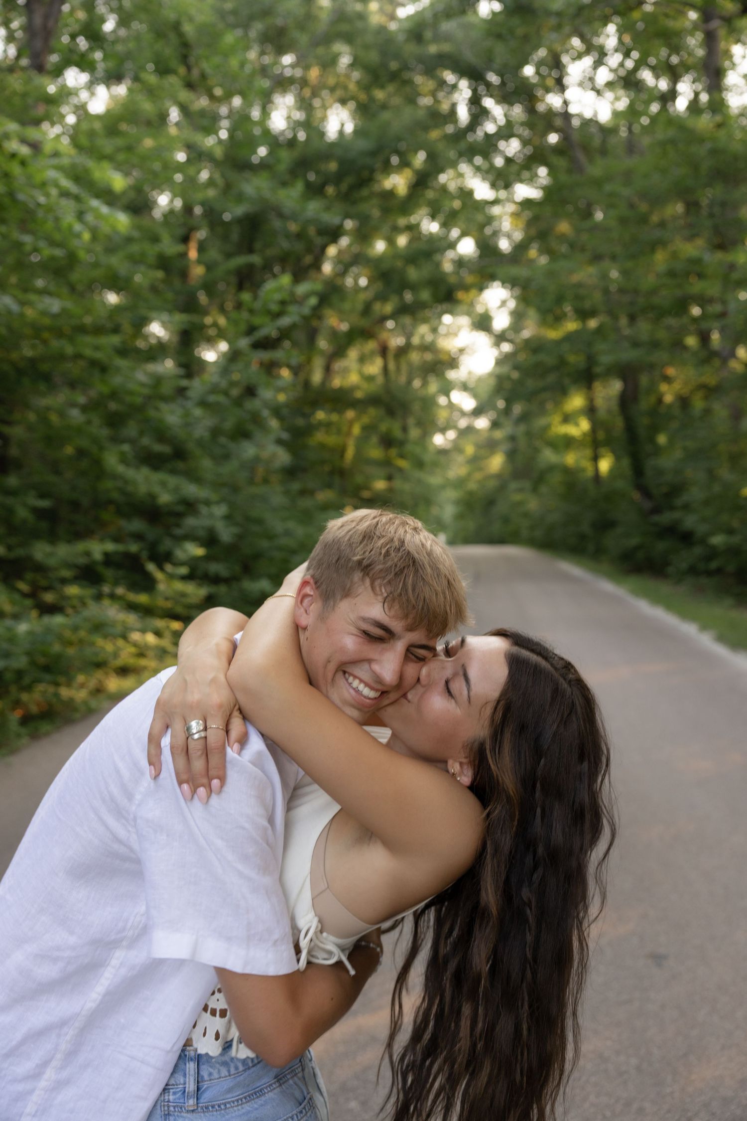 A romantic couple embracing on a tree-lined path during golden hour.