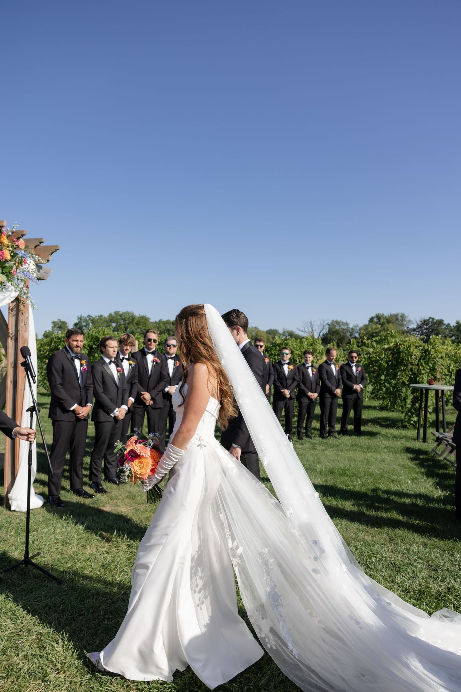 Outdoor vineyard wedding ceremony with wedding party and guests in attendance.