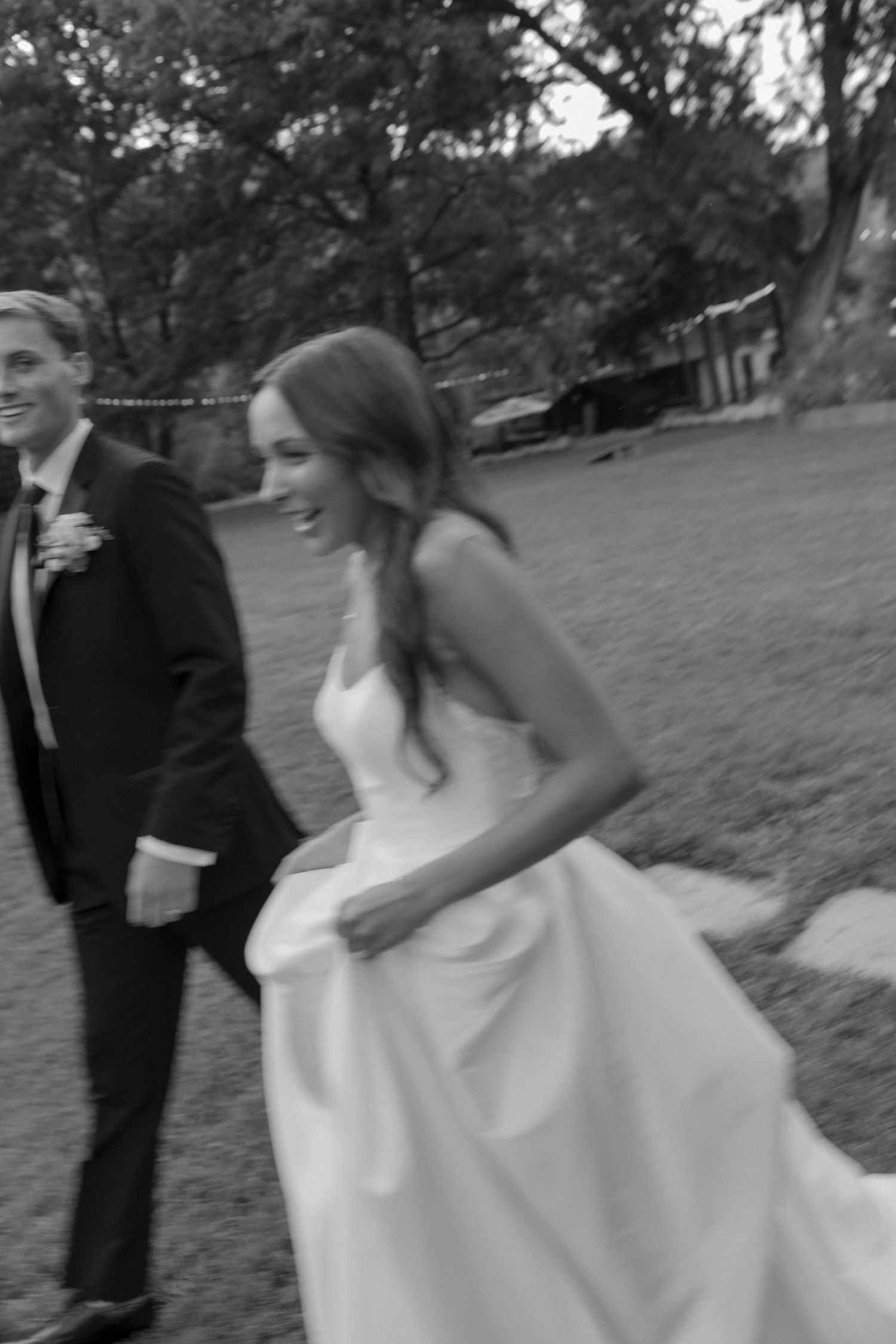 Black and white candid shot of couple walking outdoors during wedding celebration.