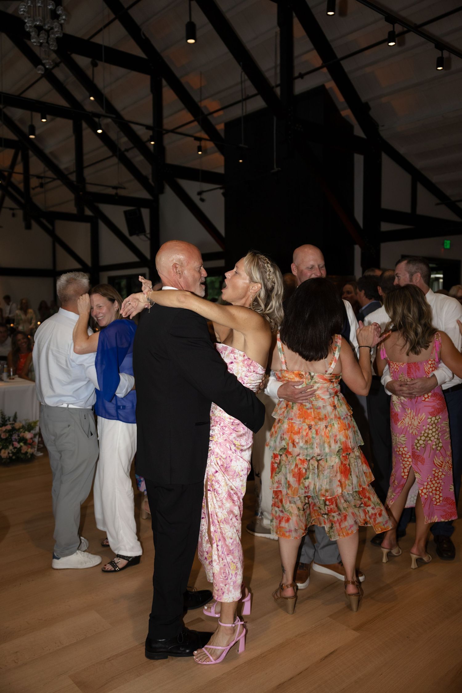 Couples slow dance on wooden floor during evening wedding reception.