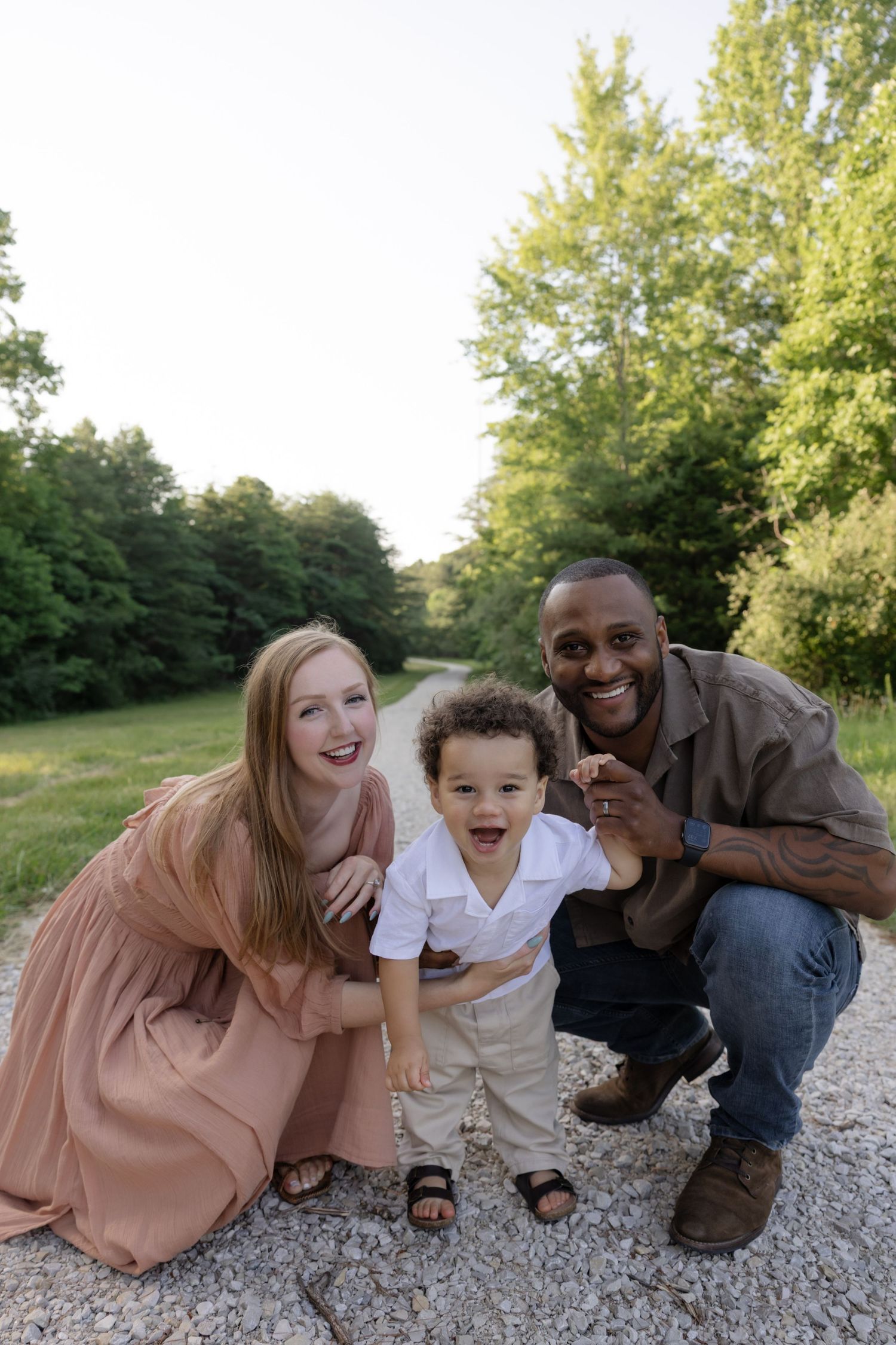 Family relaxing together on a gravel path surrounded by green trees on a sunny day.