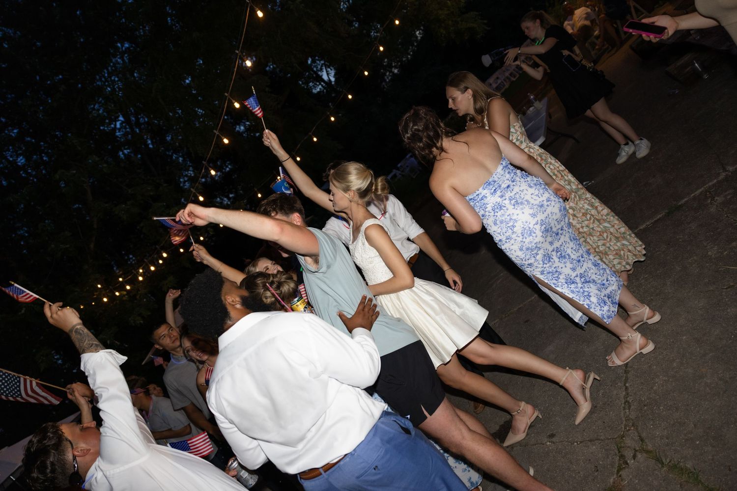People dancing and moving at outdoor party in dark setting.