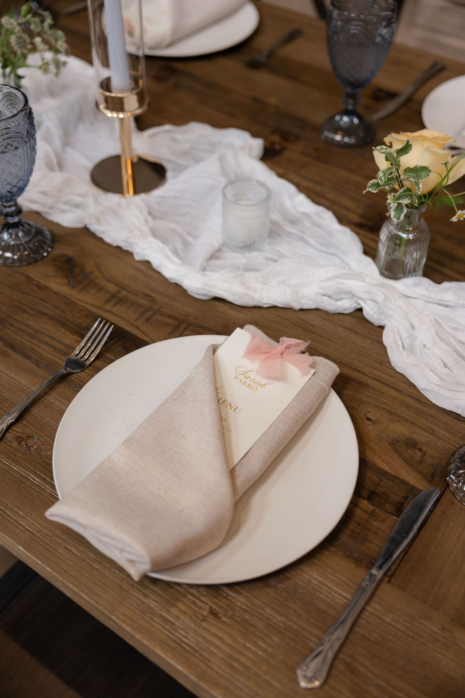 Rustic wedding table setting with white plates, linen napkins, and wooden table details.