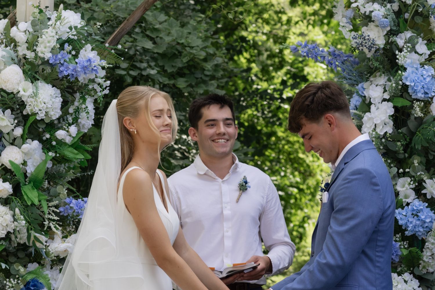 Emotional moments during a wedding ceremony under a floral-decorated arch in a garden setting.