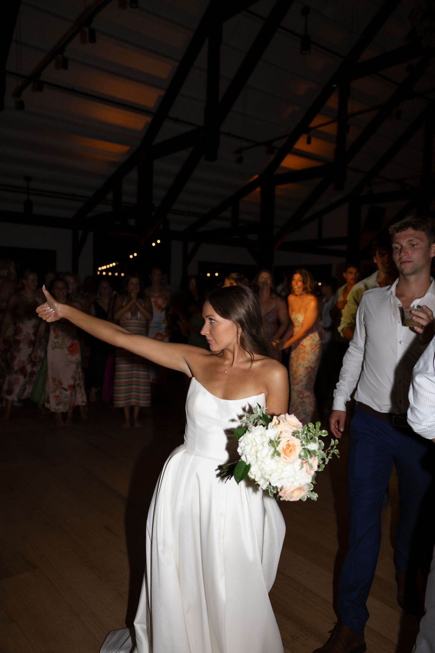 A bride in a white dress holds a bouquet while dancing at her wedding reception.