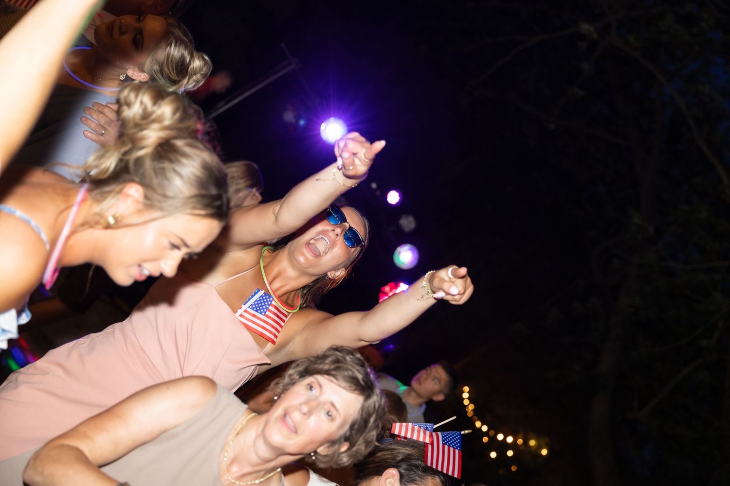 Nighttime celebration with people dancing under purple lights.