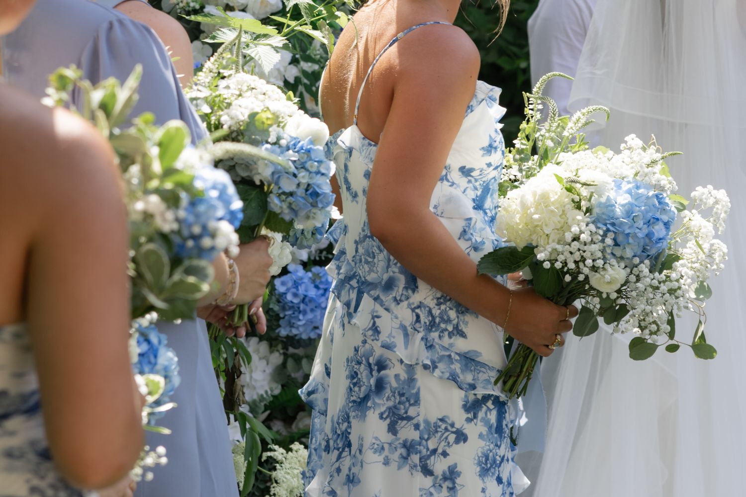 Close-up details of wedding bouquets featuring blue and white flowers held by bridesmaids.