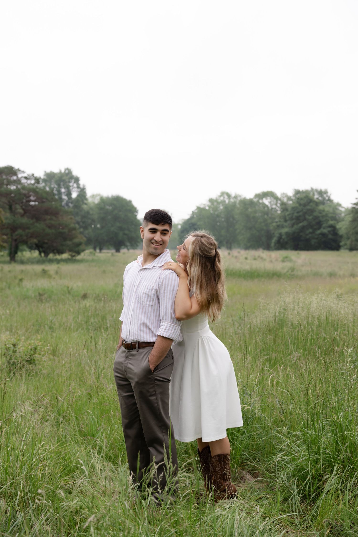 Couple in casual attire embracing in tall grass meadow.