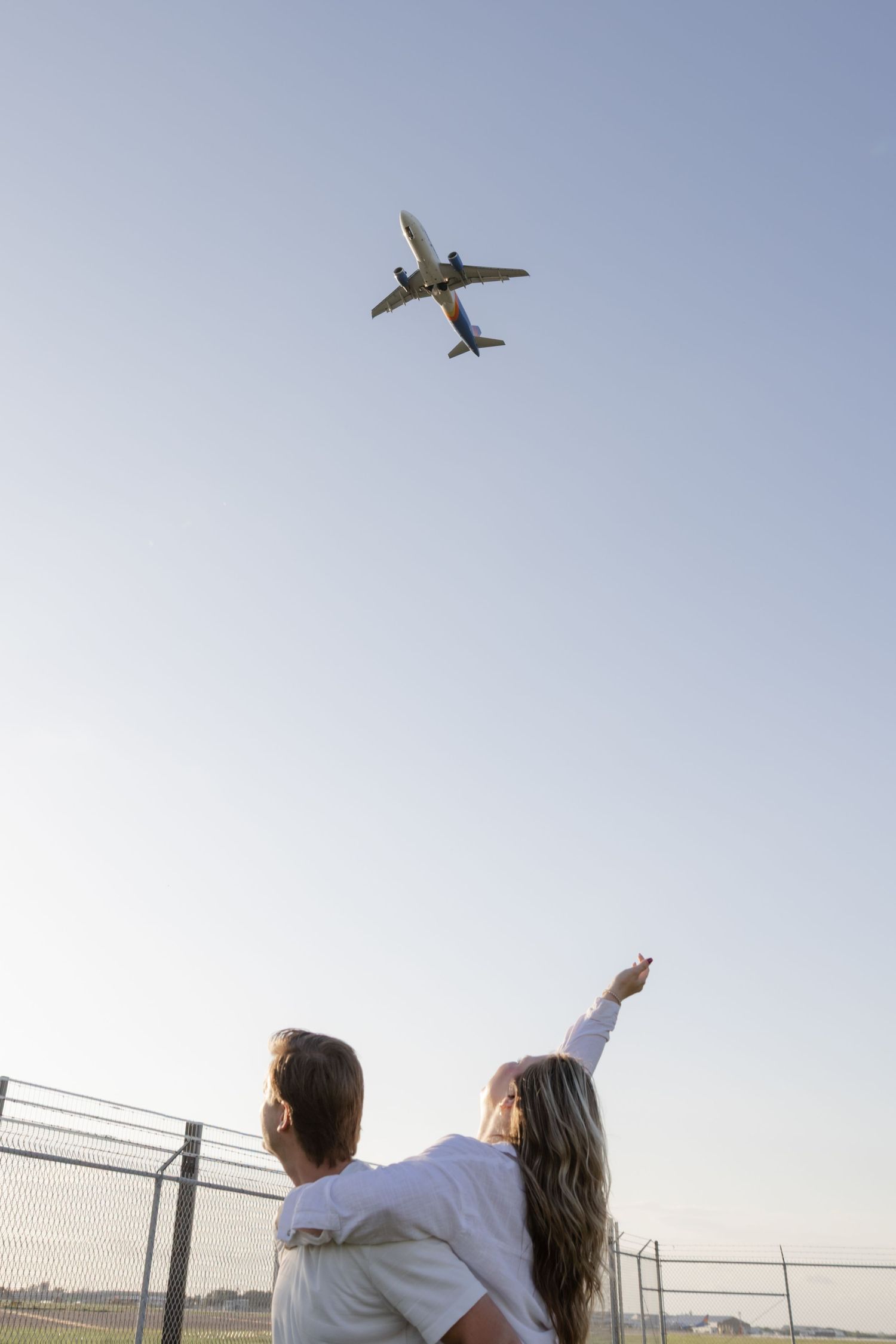 Couple pointing at airplanes flying overhead in the blue sky.