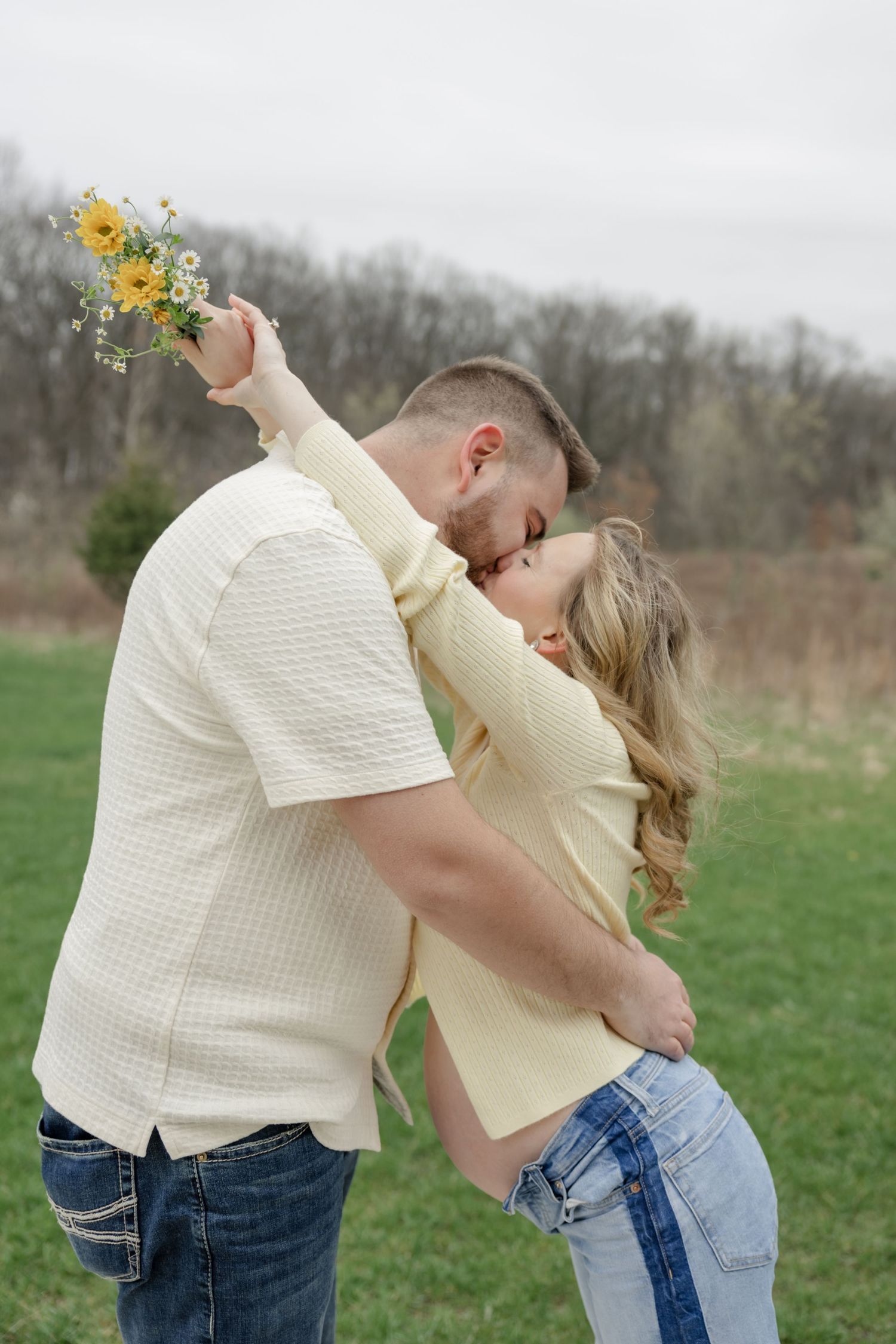Romantic couple posing with yellow wildflowers during outdoor maternity photoshoot.