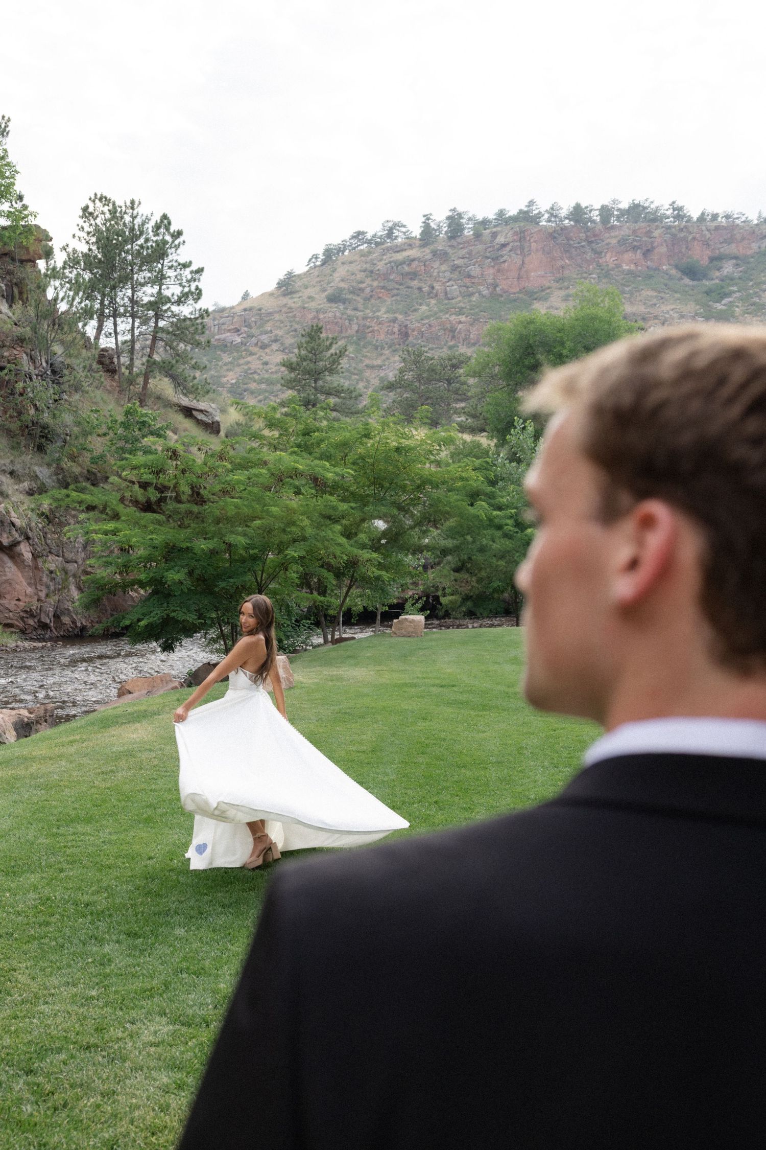 Wedding couple runs playfully across a grassy lawn with mountains in the background.