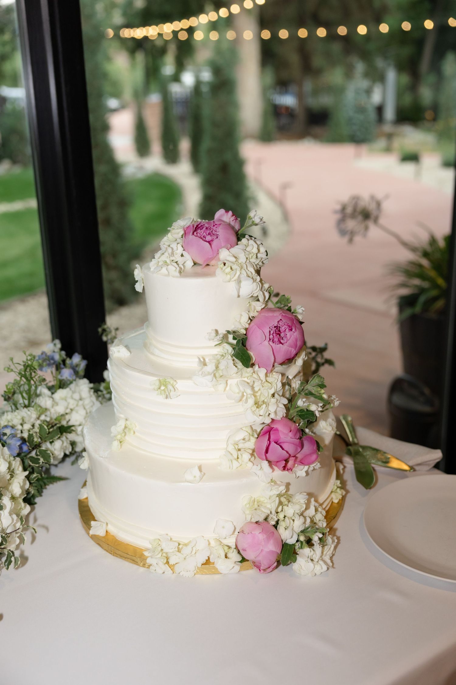 White tiered wedding cake decorated with fresh pink peonies and delicate floral accents.